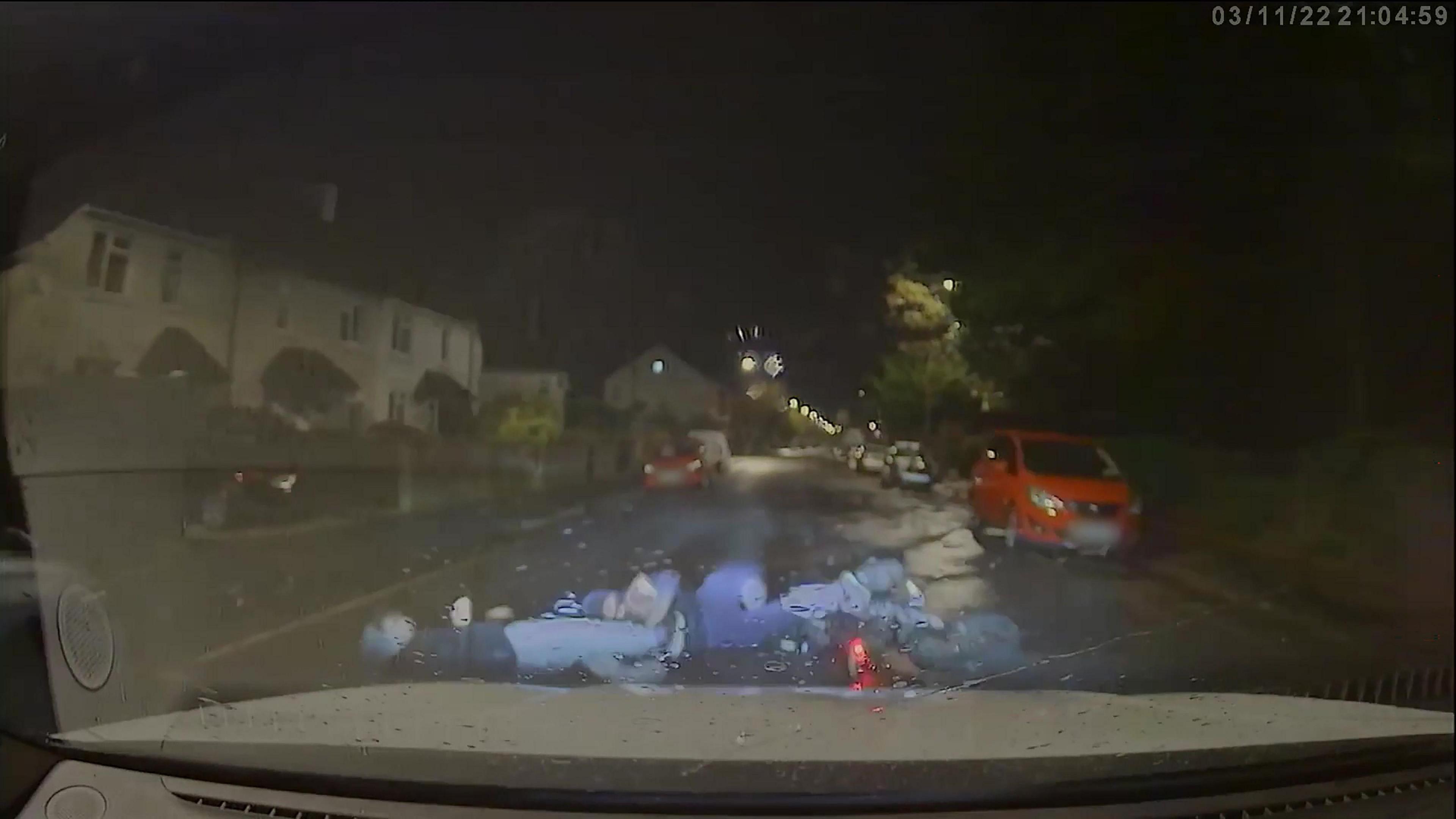 A dashcam shot of two people lying in the road after a police car drove into them