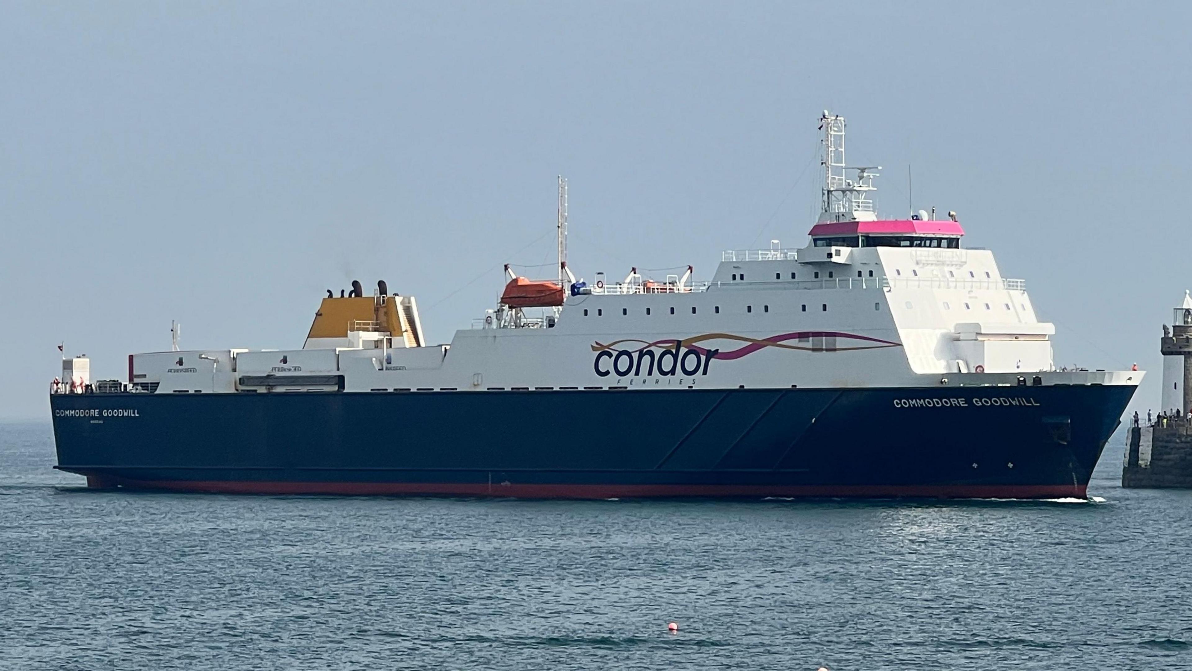 A white, blue and pink Condor Ferries boat in the water as it heads into a harbour on a sunny day.