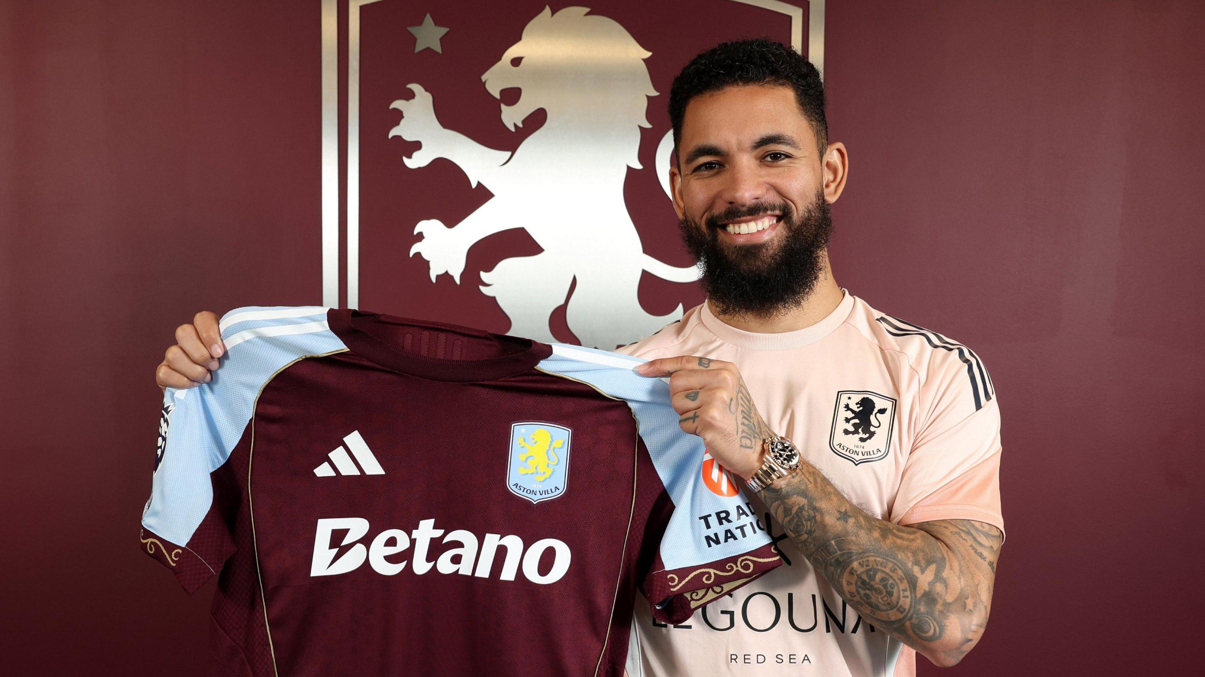 Douglas Luiz smiles as he holds up the Aston Villa shirt at his signing