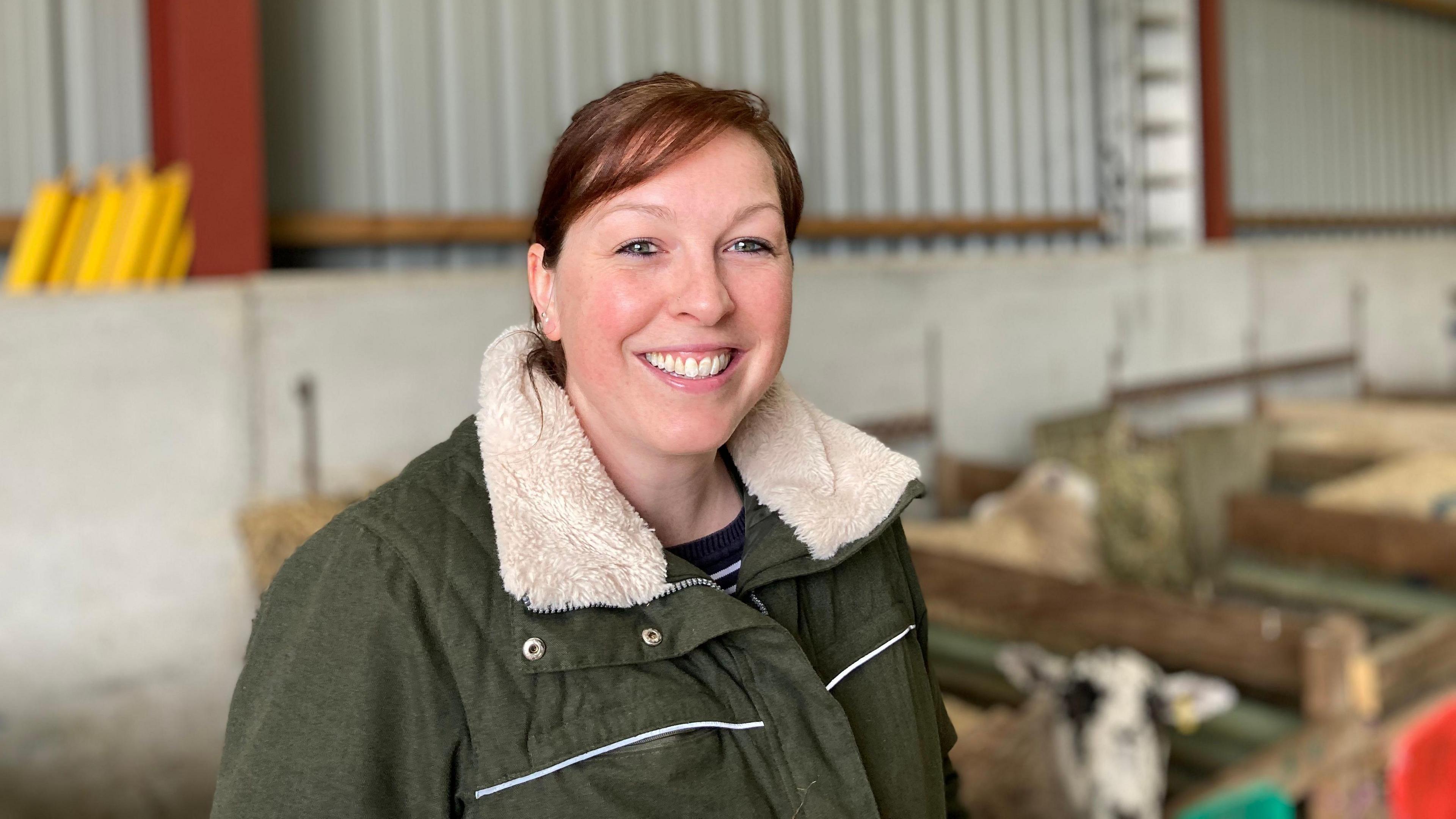 Rosie Jeffries stands in a barn with several ewes standing behind her