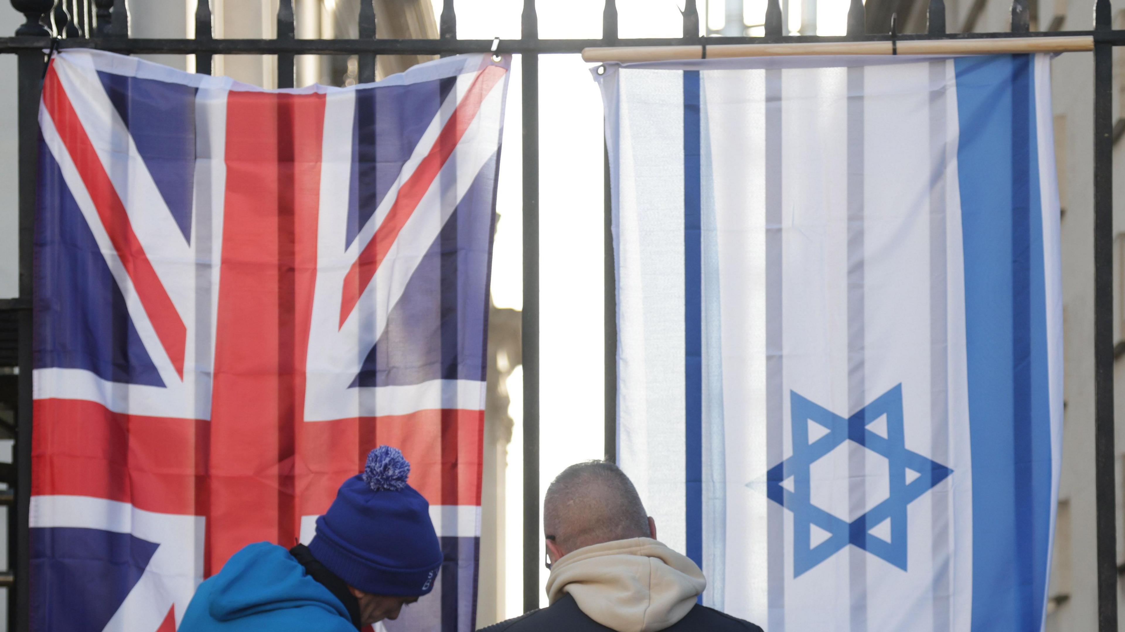 Two people putting up a Union Jack flag and Israeli flag on a railing.