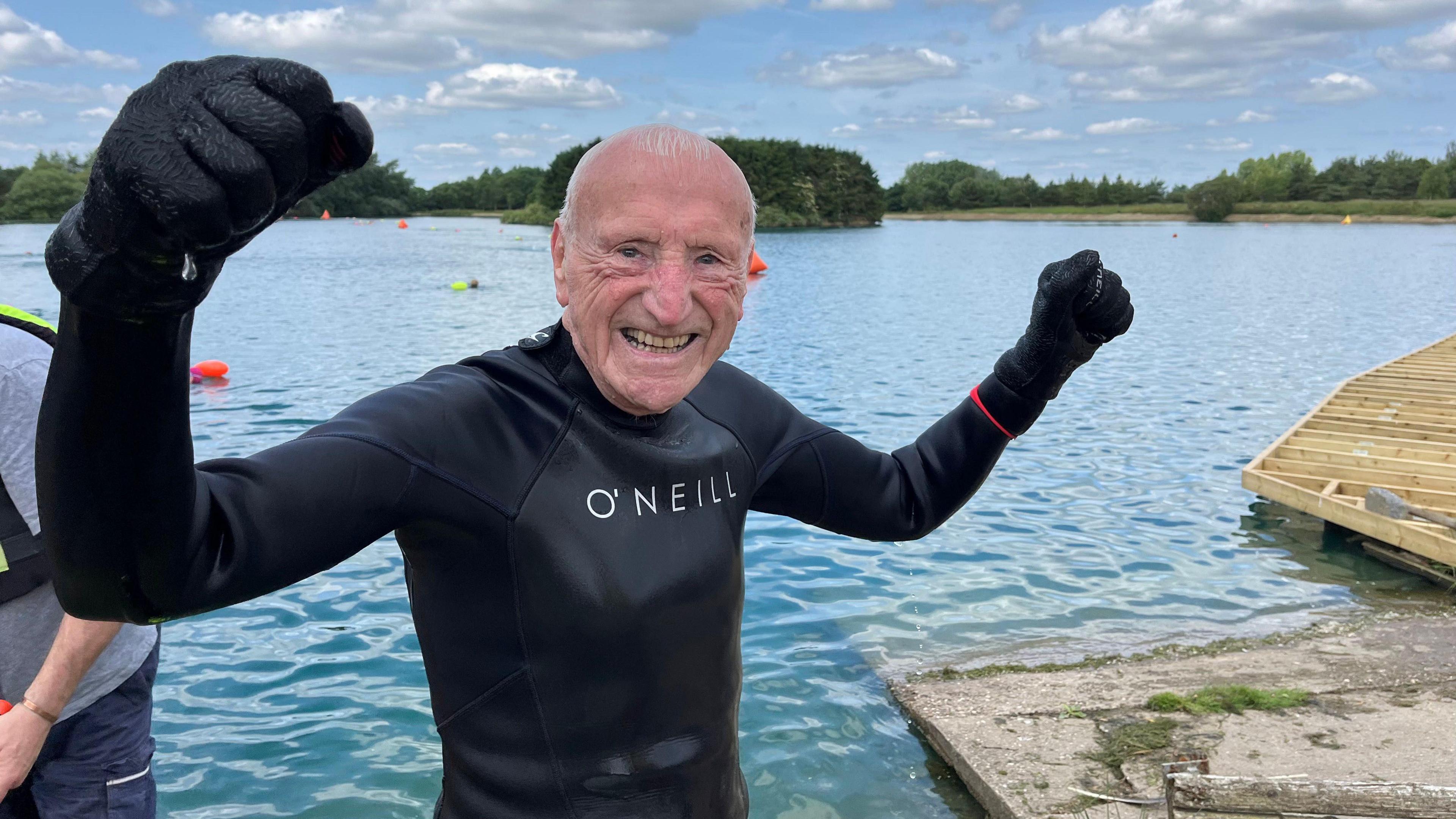 David stands with fists raised in the air with the lake behind him