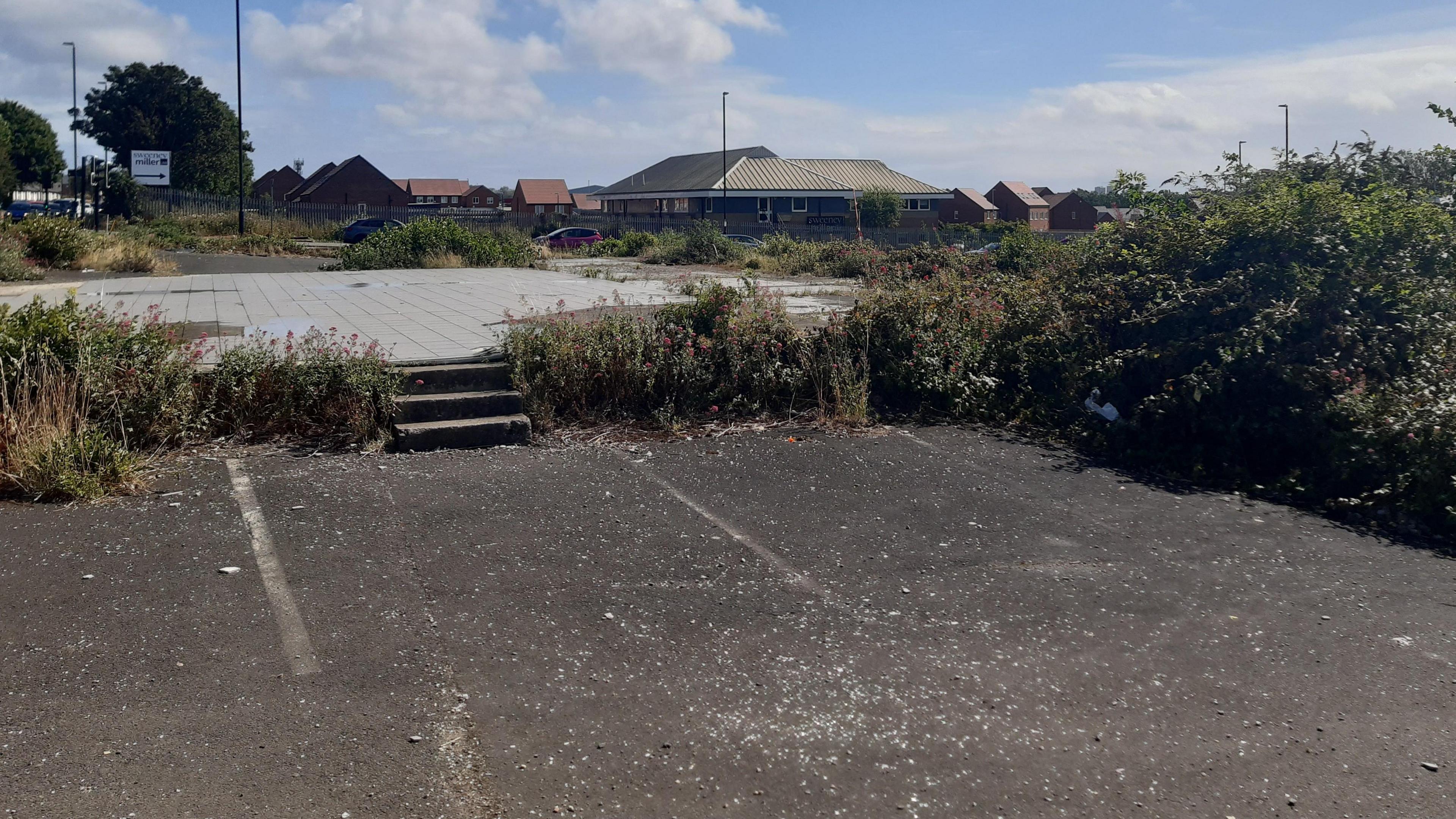 A concrete forecourt with steps in the middle leading to another concrete area, the whole area is derelict. 