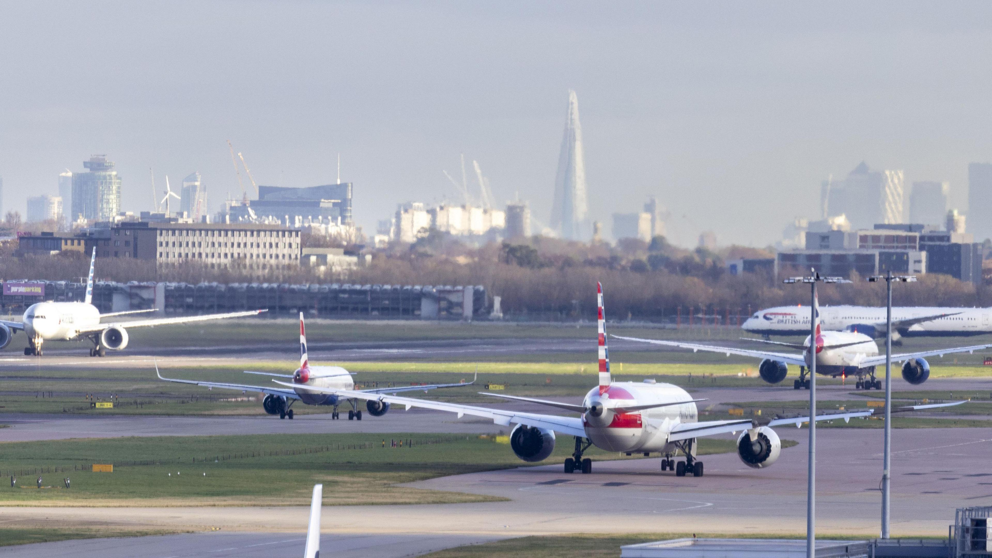 Five aircraft on runways at Heathrow Airport with London skyline in the background