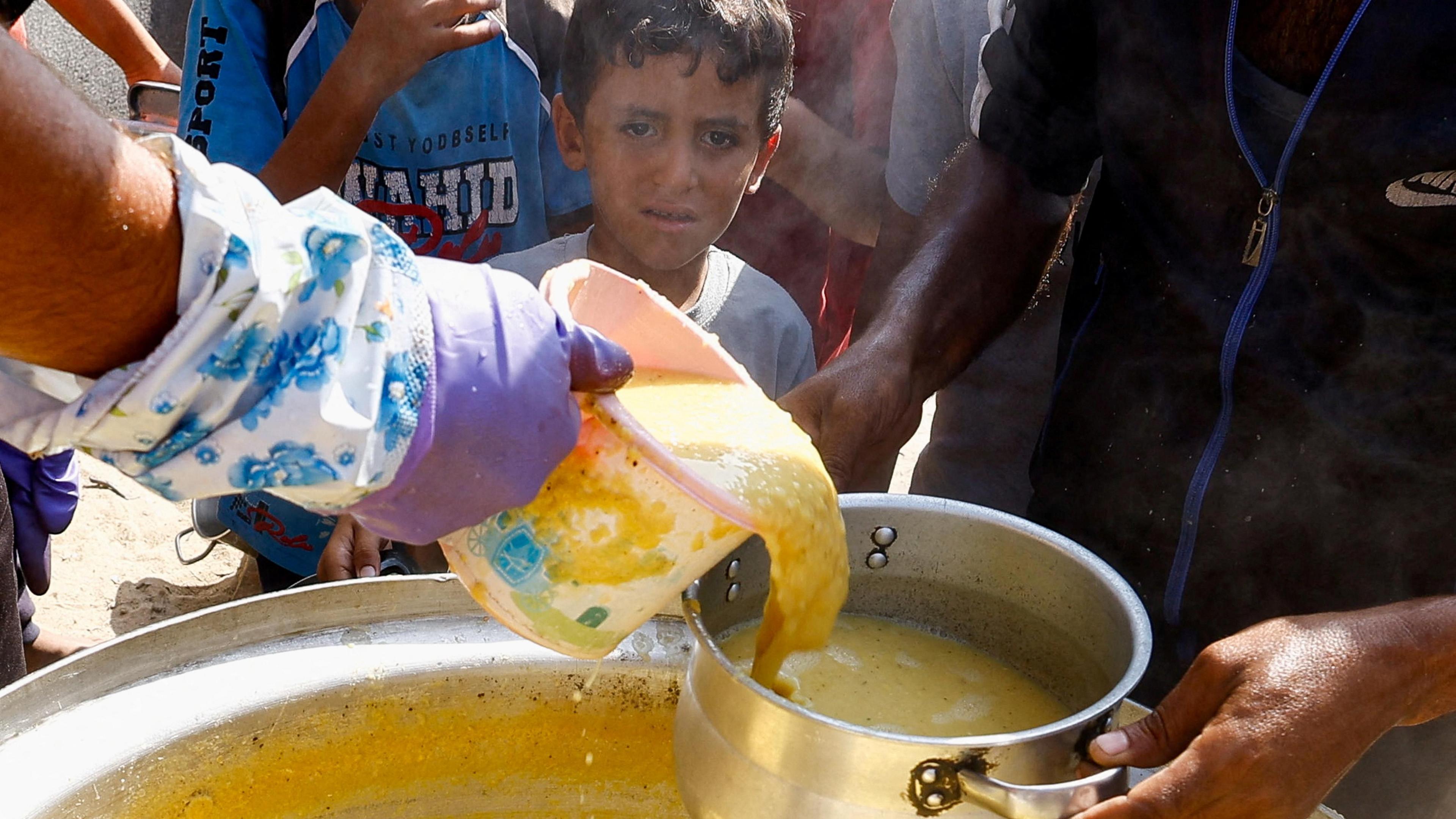 A Palestinian child looks on as food is handed out at a kitchen in Khan Younis, in the southern Gaza Strip (16 October 2024)