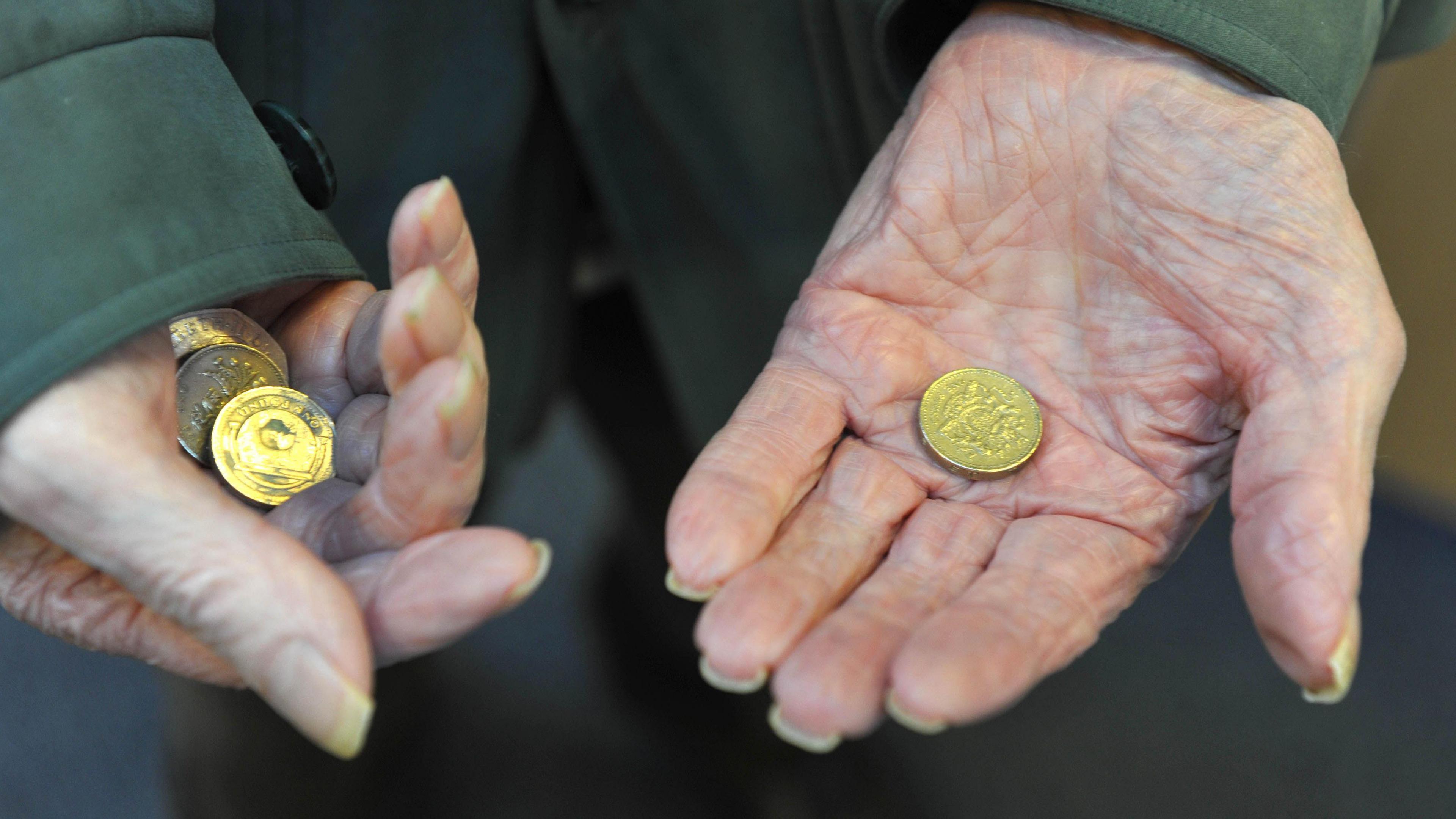 Close up of elderly person's hands holding coins. The person is wearing a green code. They have a £1 coin in their hand with a number of other coins in the other hand.