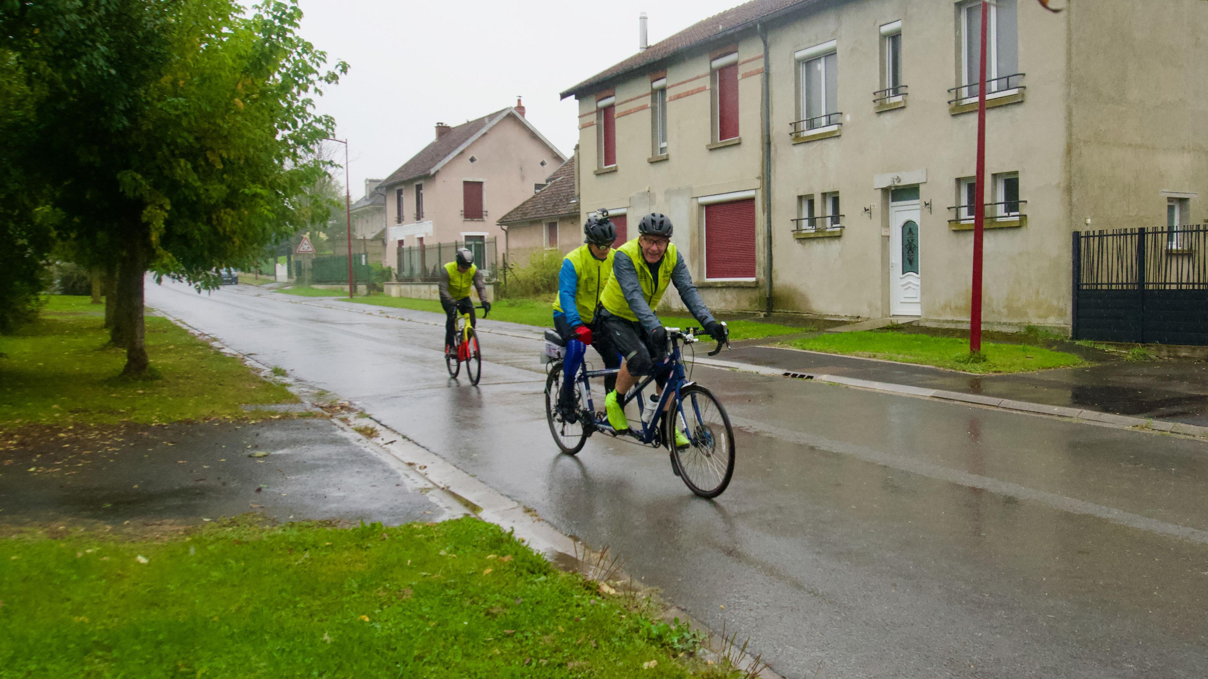 Two men on a tandem bicycle with another cyclist following behind