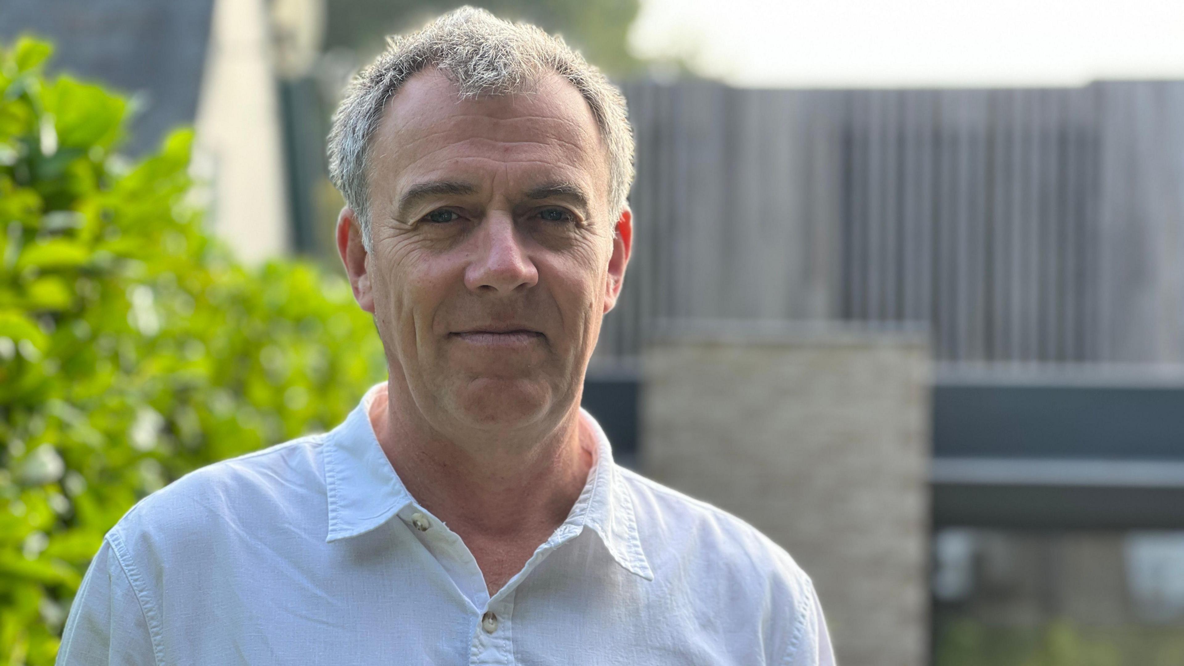 man in white shirt and grey hair standing outside house