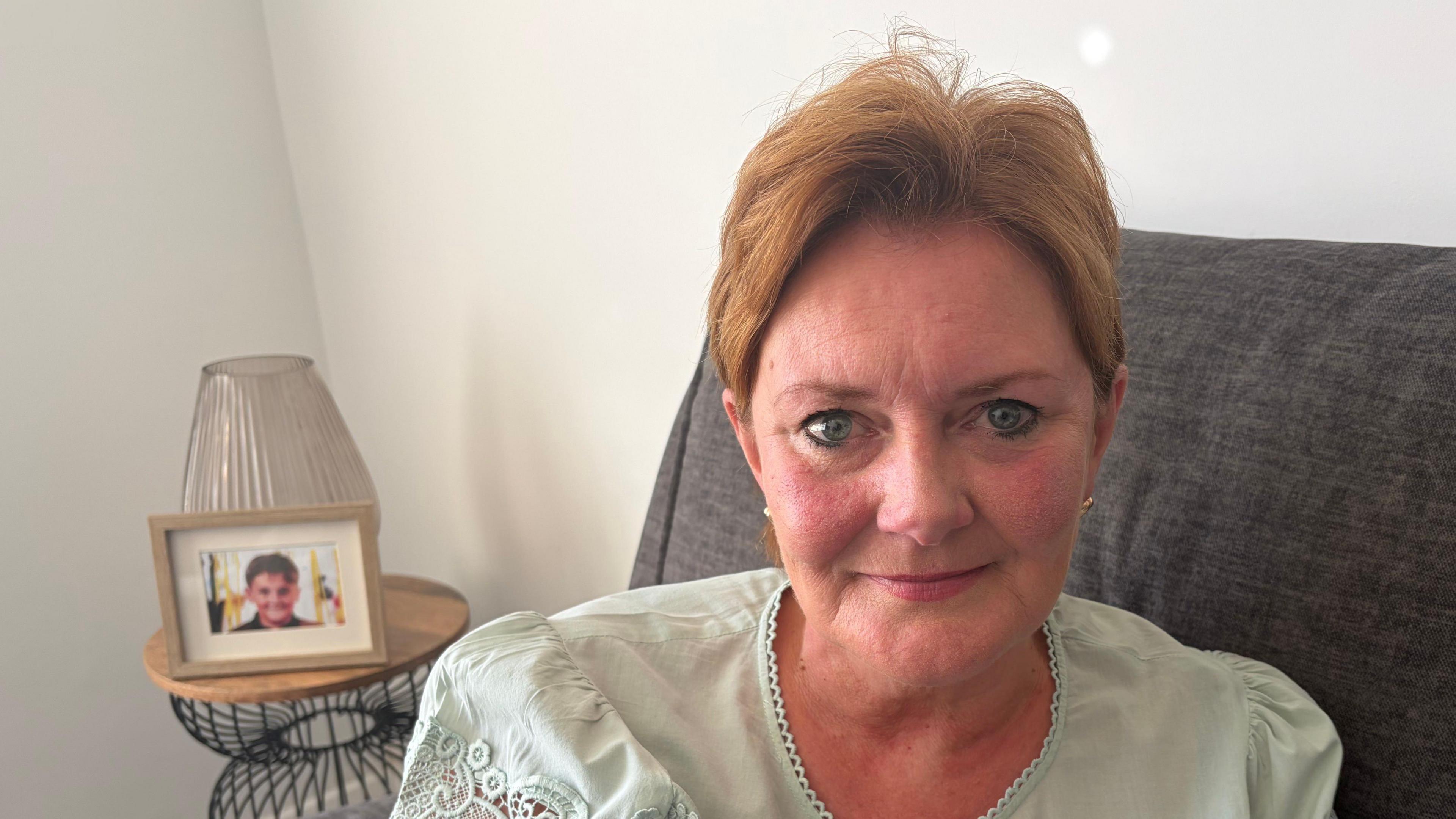 A woman with short auburn hair sitting on a sofa wearing a green top.