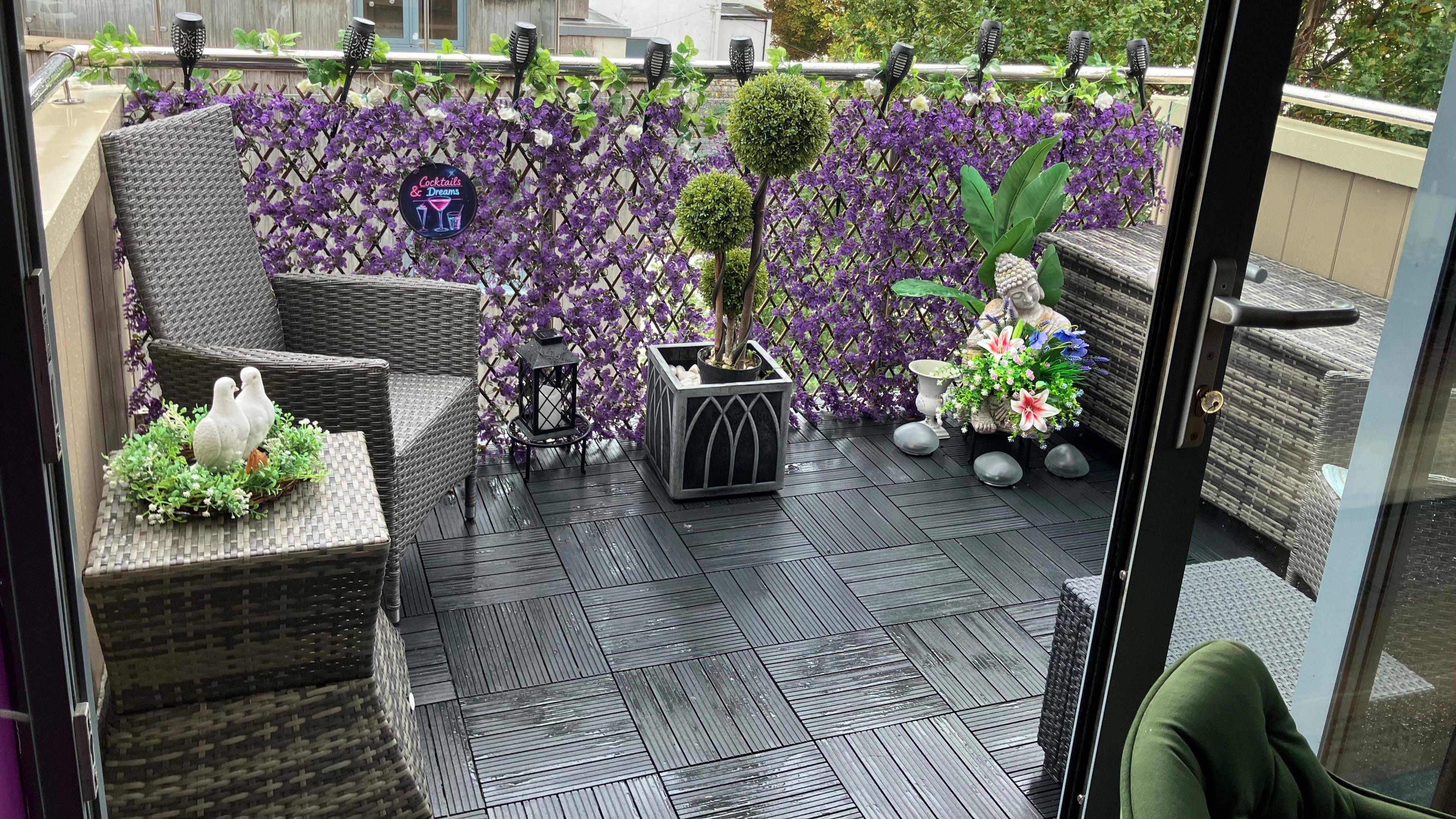 A colourful balcony with chairs, decorations and purple foliage, the decking is slightly wet due to the weather