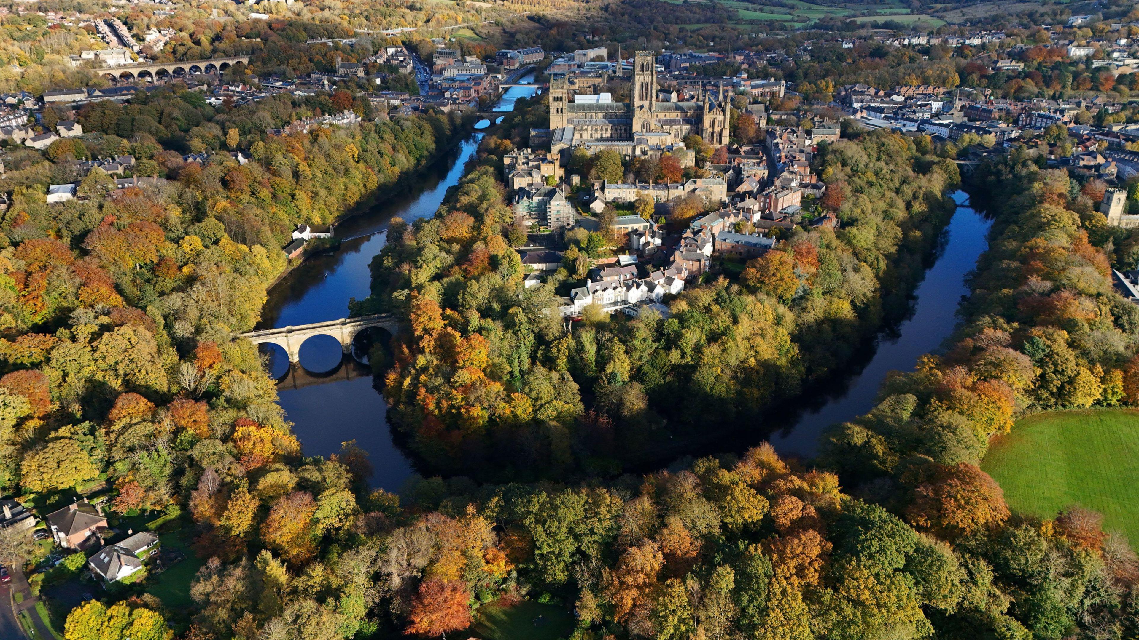 An aerial shot of Durham City. The River Wear curves around the central peninsula. Durham Cathedral can be seen among a number of other buildings.