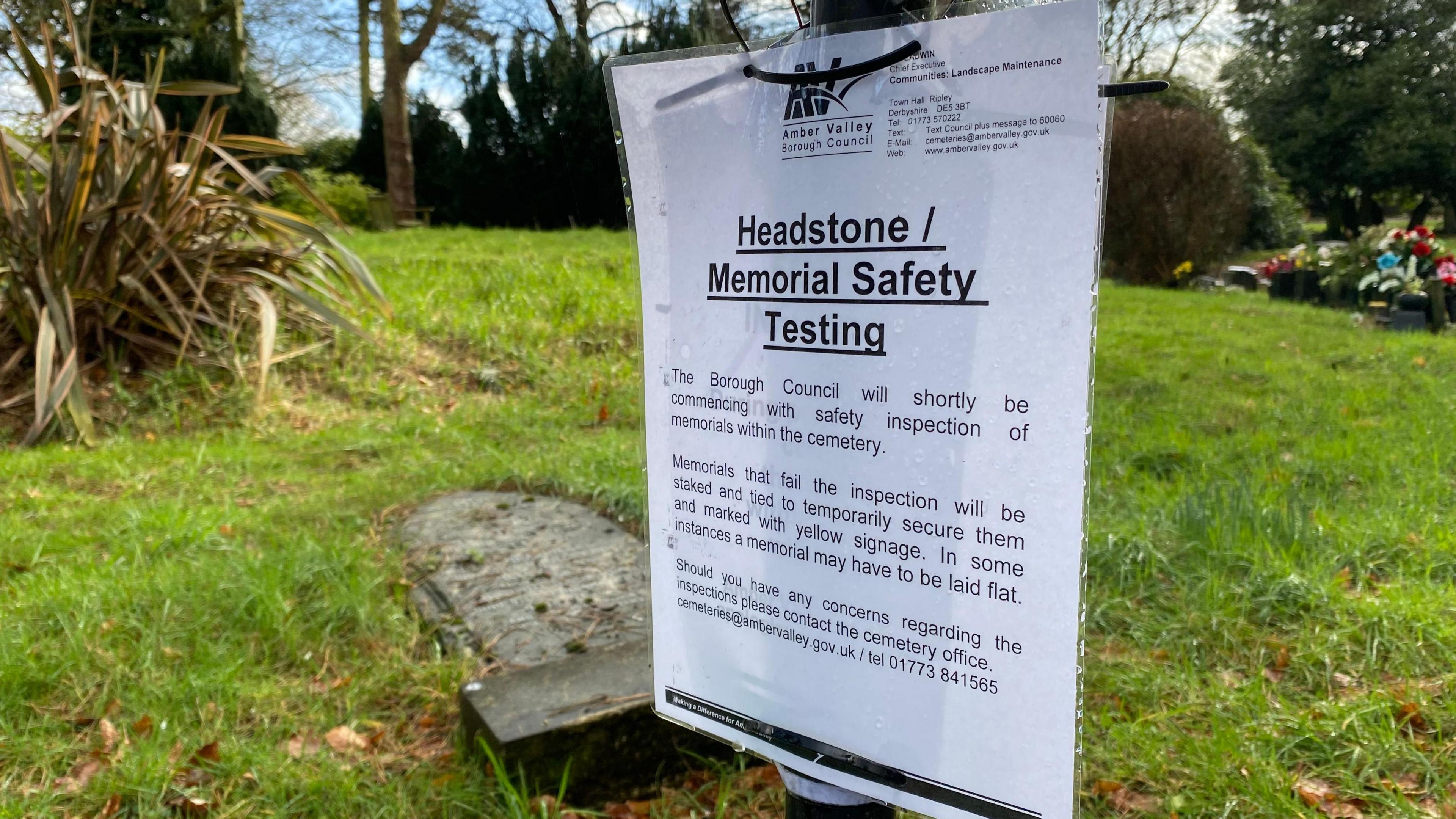 A white sign, attached to a lamppost, at the Ripley Cemetery. The sign encourages those impacted to get in touch. 