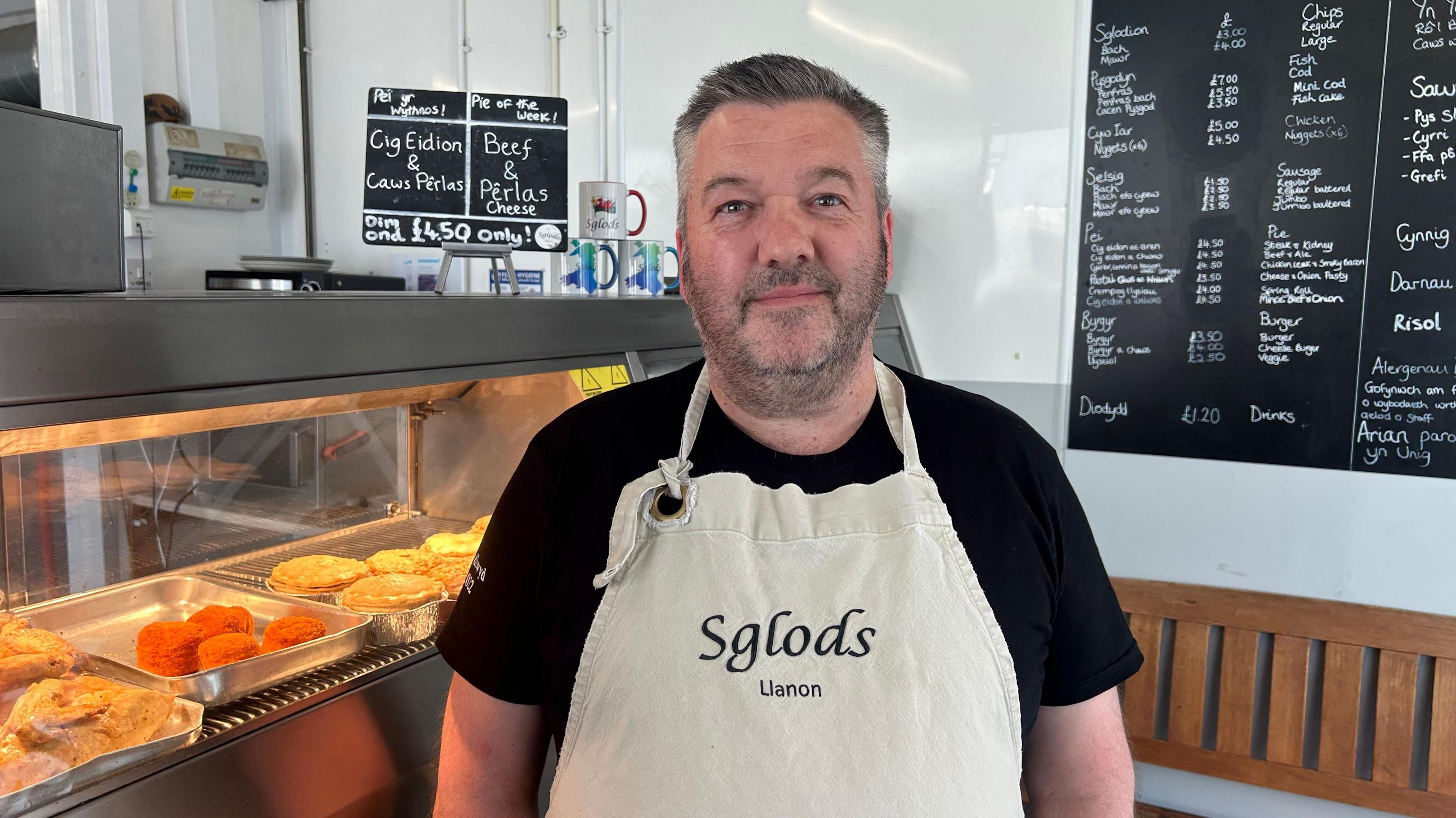 Aled Roberts o flaen y cownter yn siop Sglods Llanon