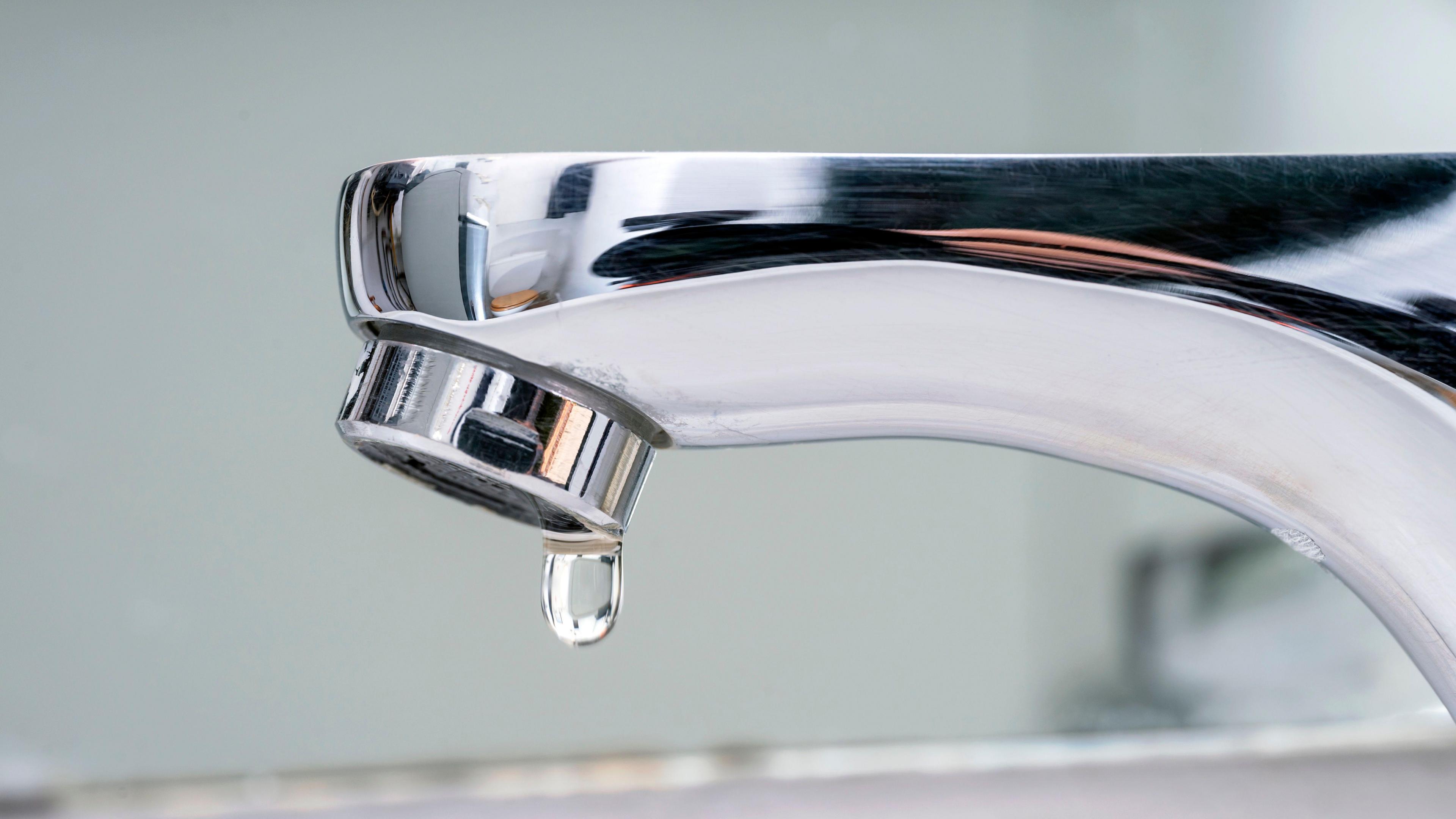 A silver tap with a small drop of water.