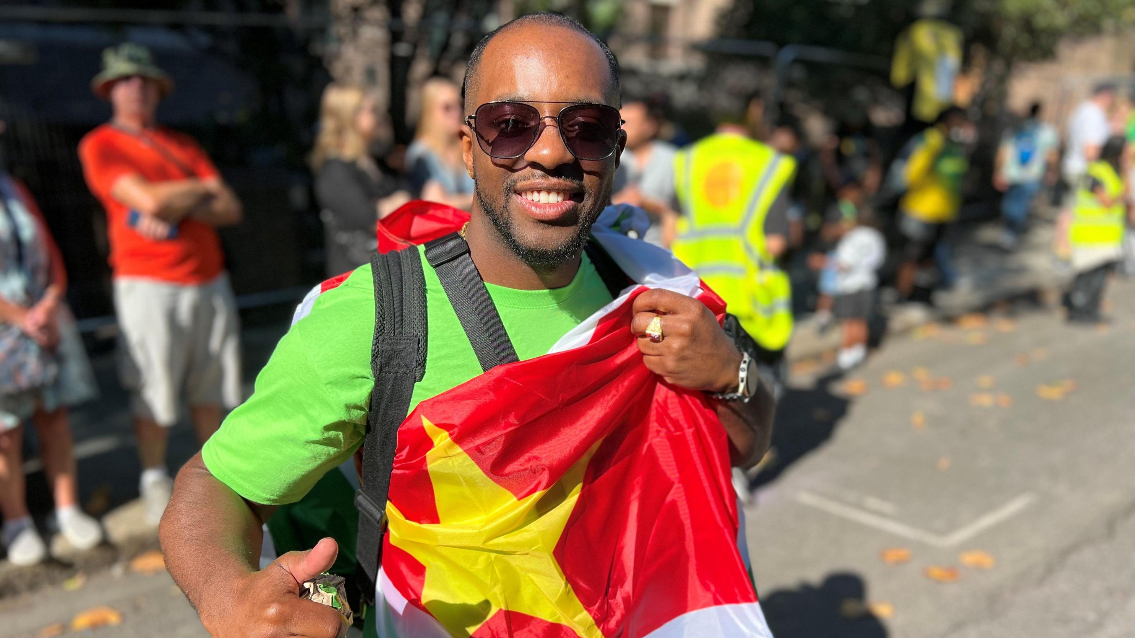 Derillio Alexander in a green t-shirt and sunglasses, holding a flag.