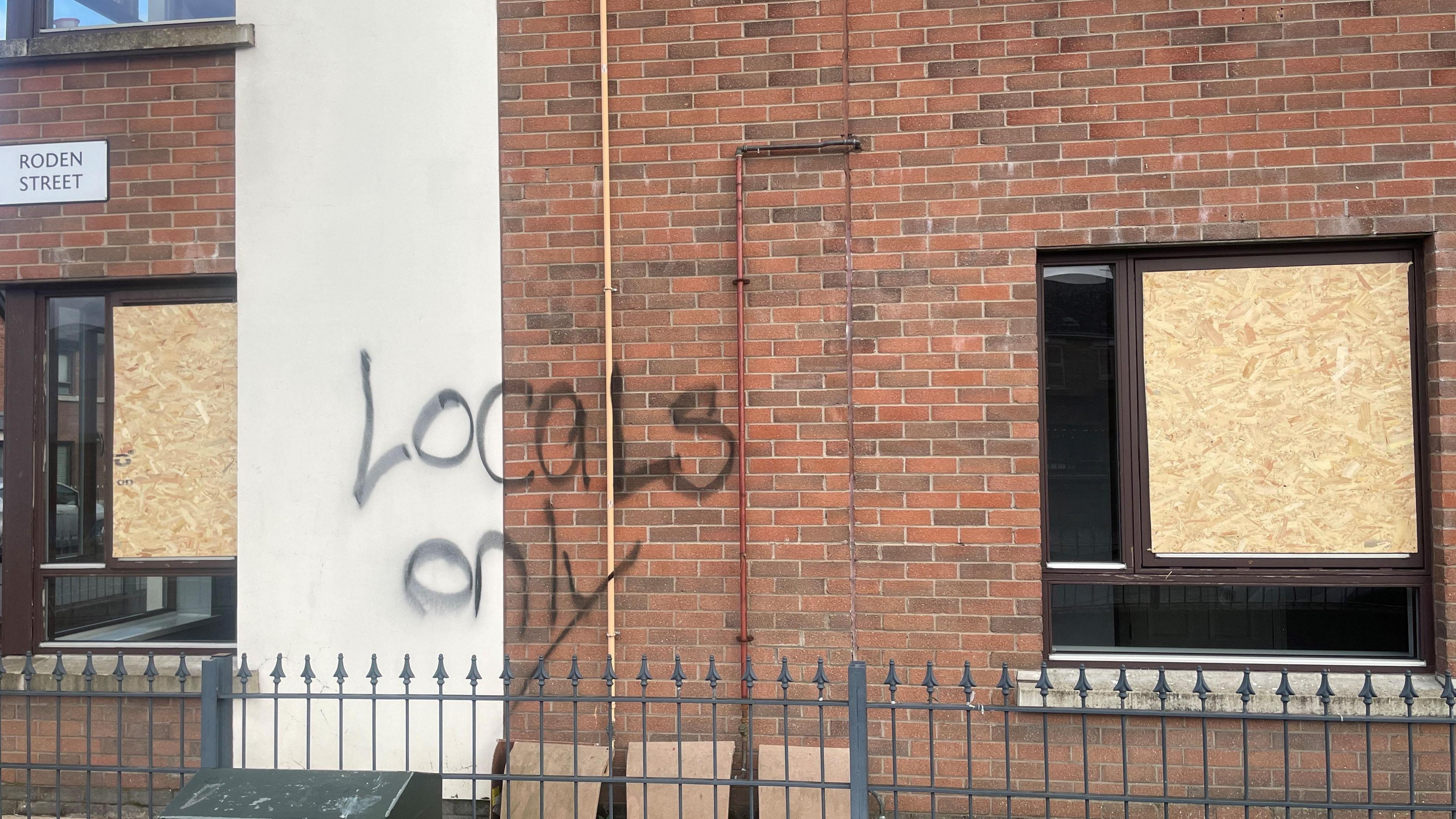 A flat with windows boarded up. Graffiti has been daubed with graffiti saying locals only.