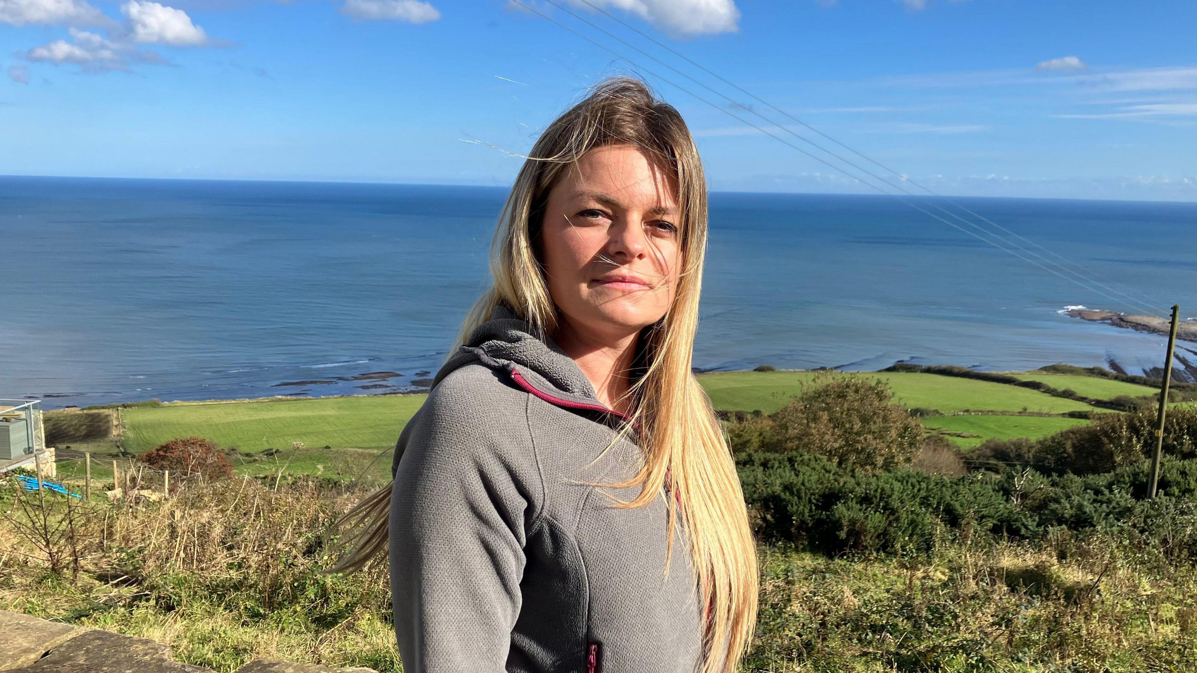 A woman with long blonde hair stands overlooking the sea at Robin Hood's Bay