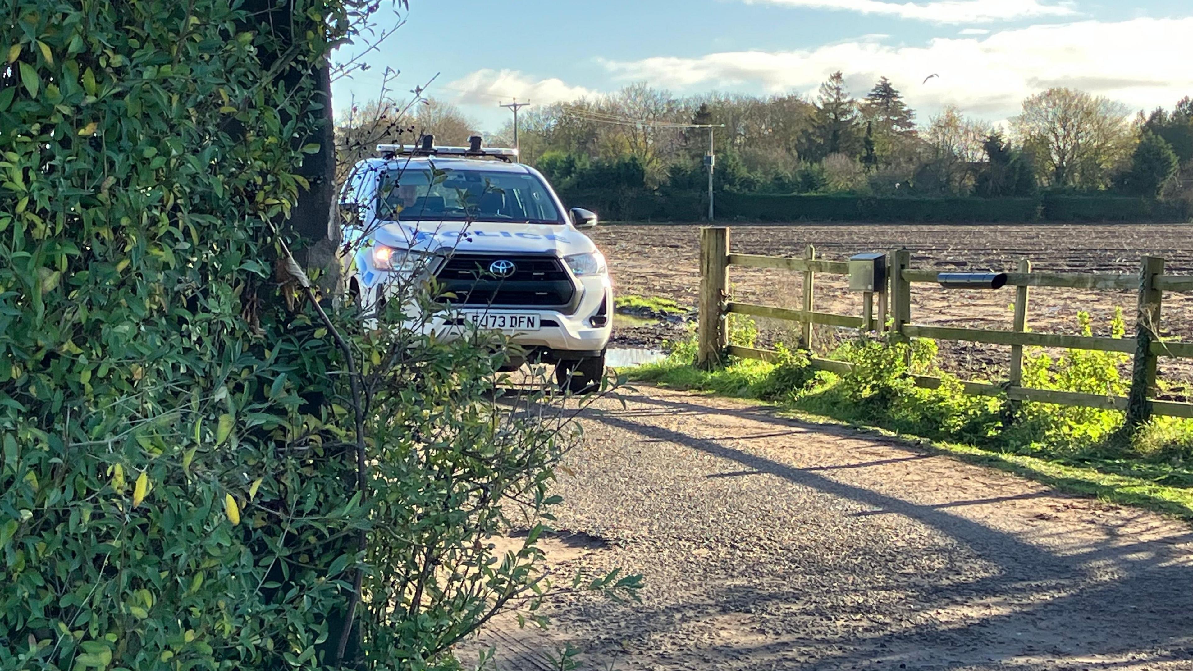 A police vehicle is parked at the entrance to a farm