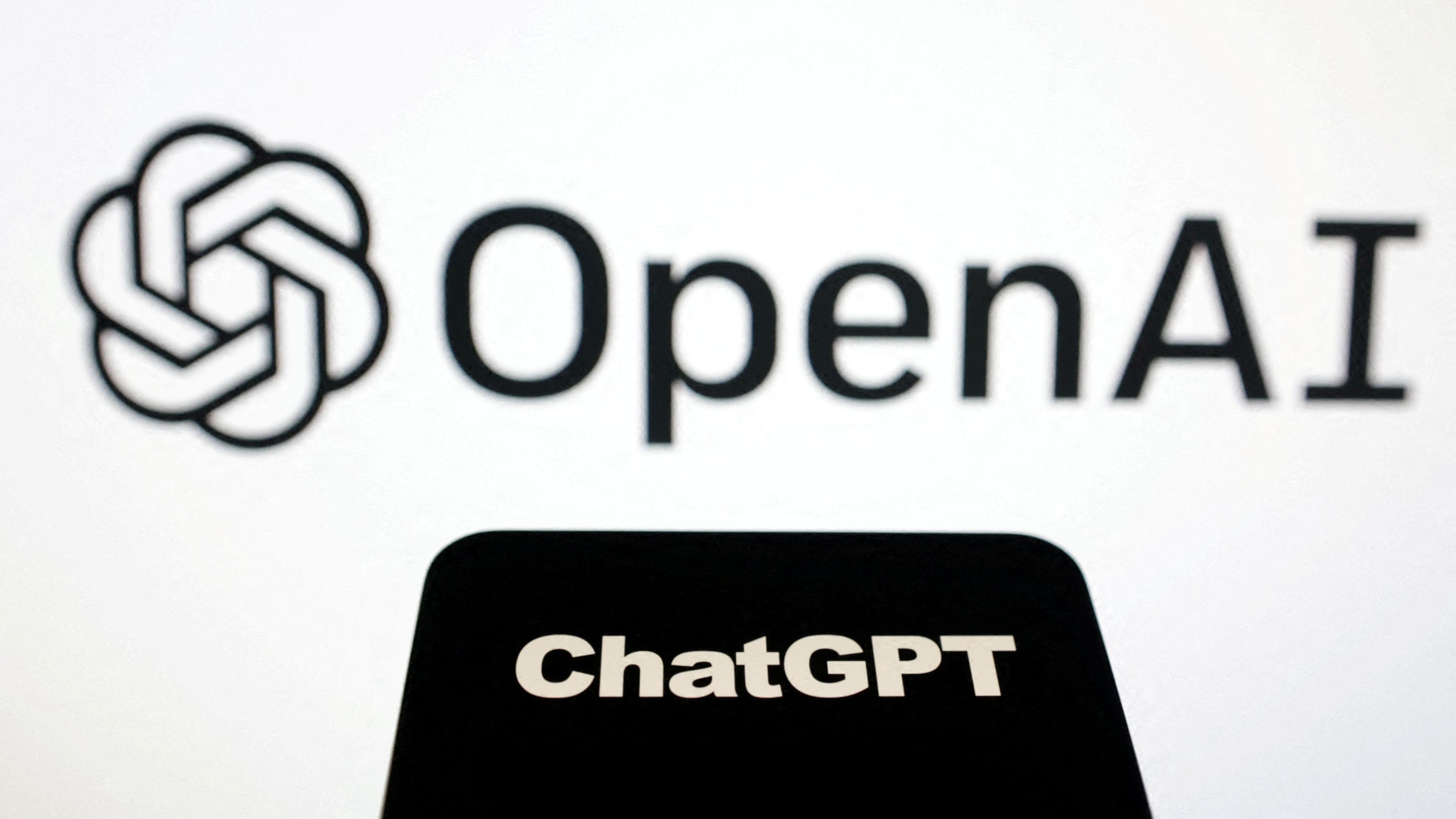 The OpenAI logo on a large white screen, with the ChatGPT logo on a black phone face in front of it.