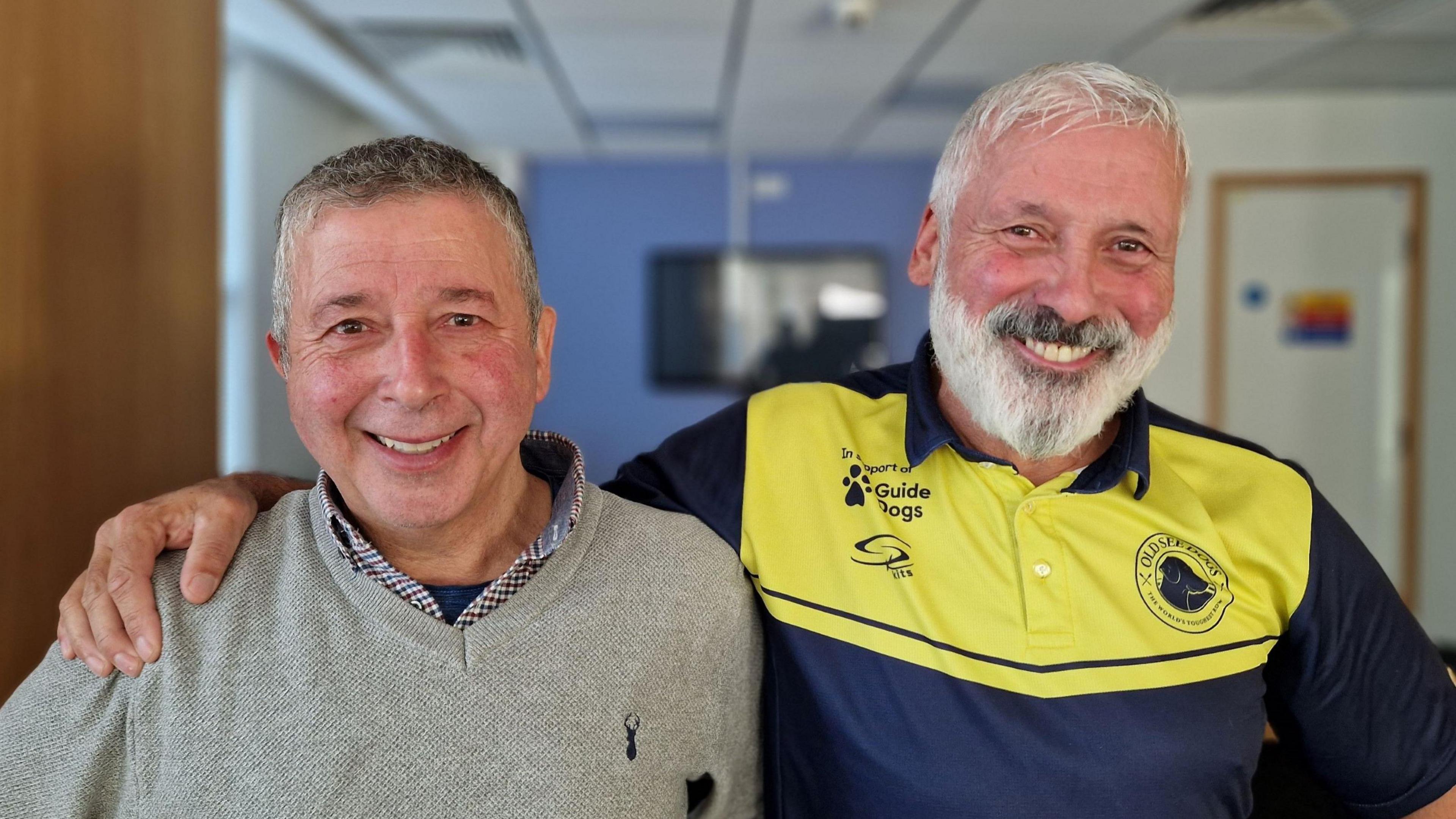 Two men, one in a grey jumper and one in a blue and yellow t-shirt