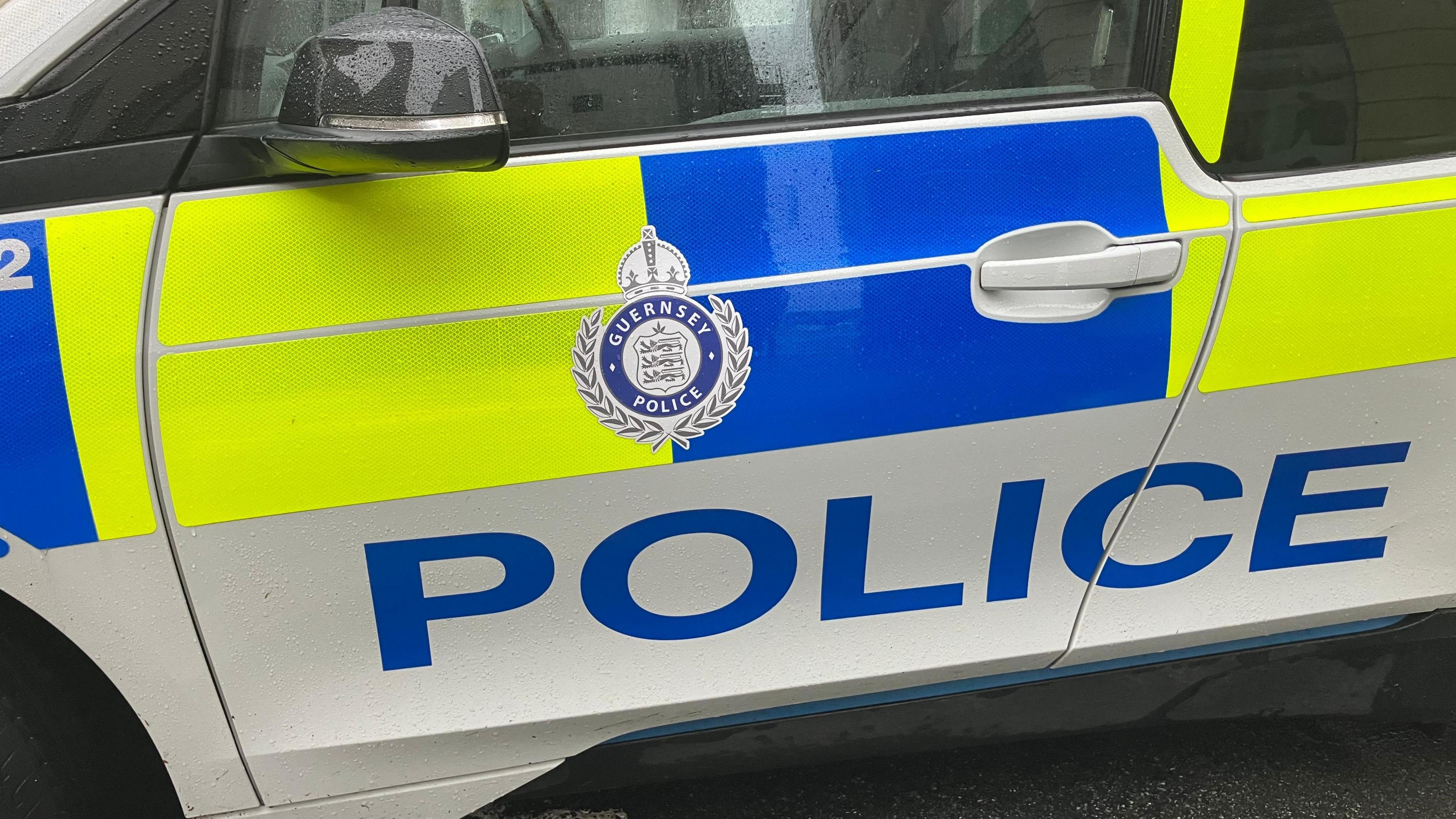 A close-up photo of the white, fluorescent green and blue door of a police car which reads 'Police' and has the Guernsey Police logo above it.