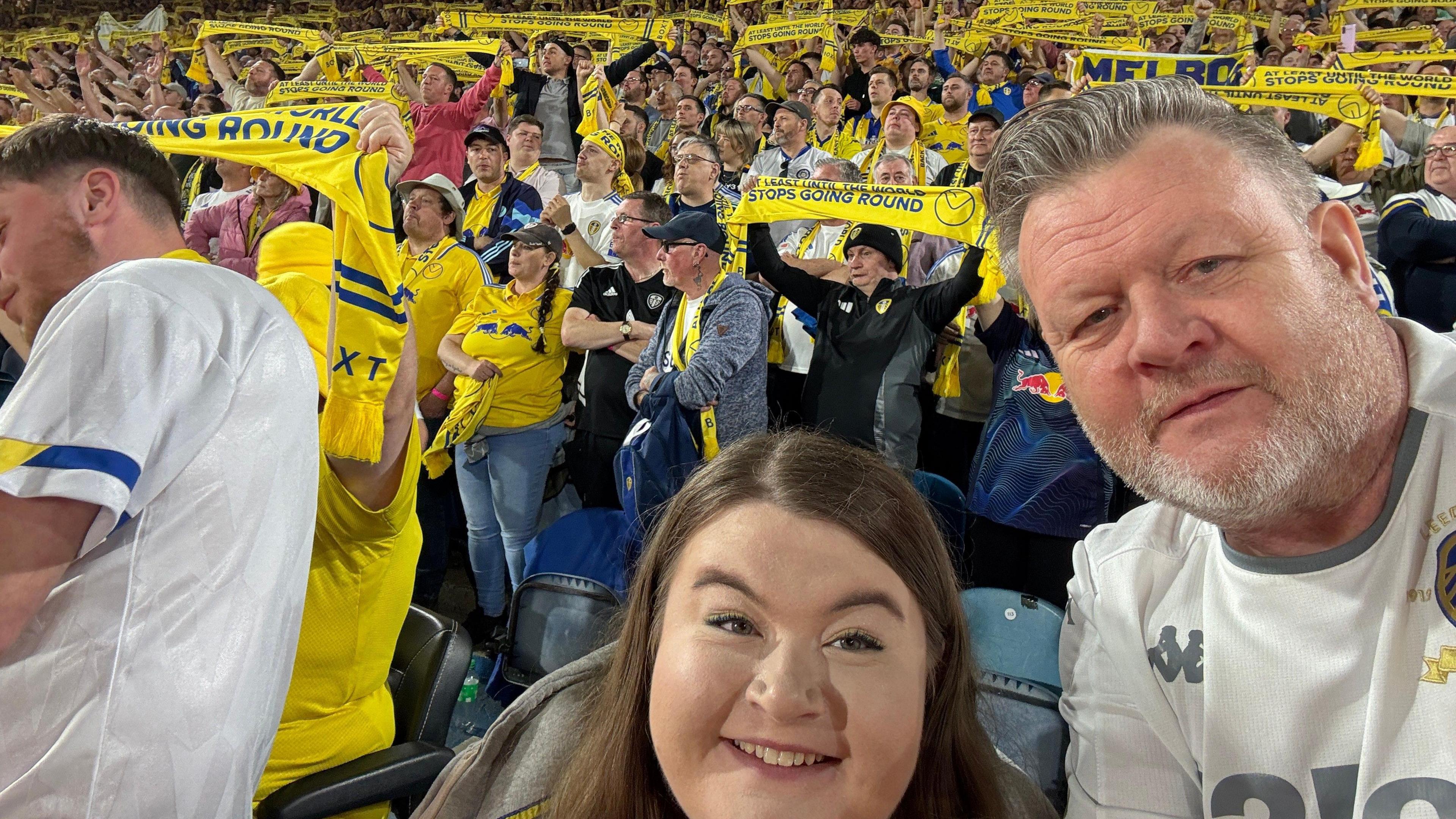 An image of a father and daughter posing for a selfie among hundreds of Leeds United scarves