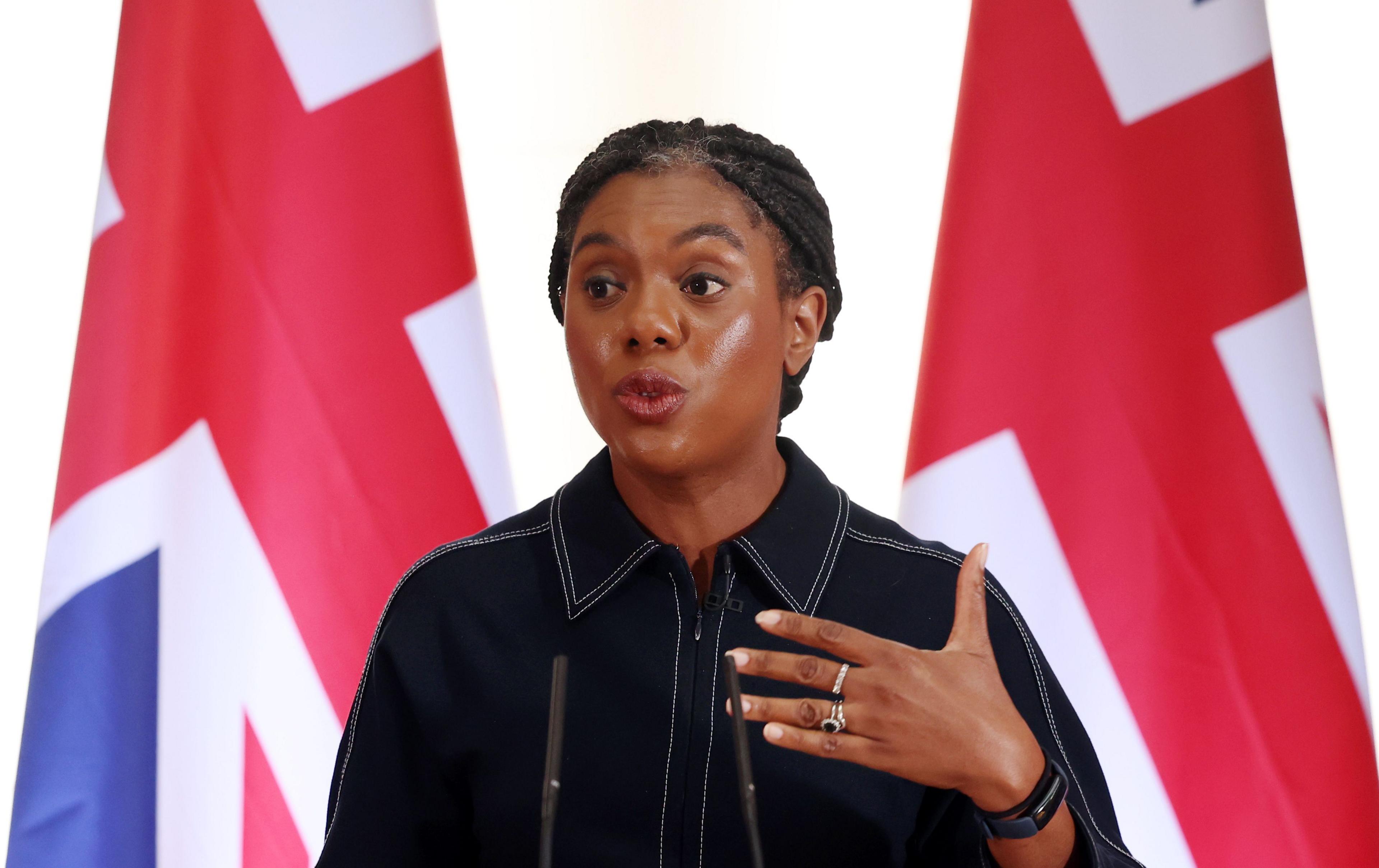 Kemi Badenoch giving a speech in front of two Union Jacks.