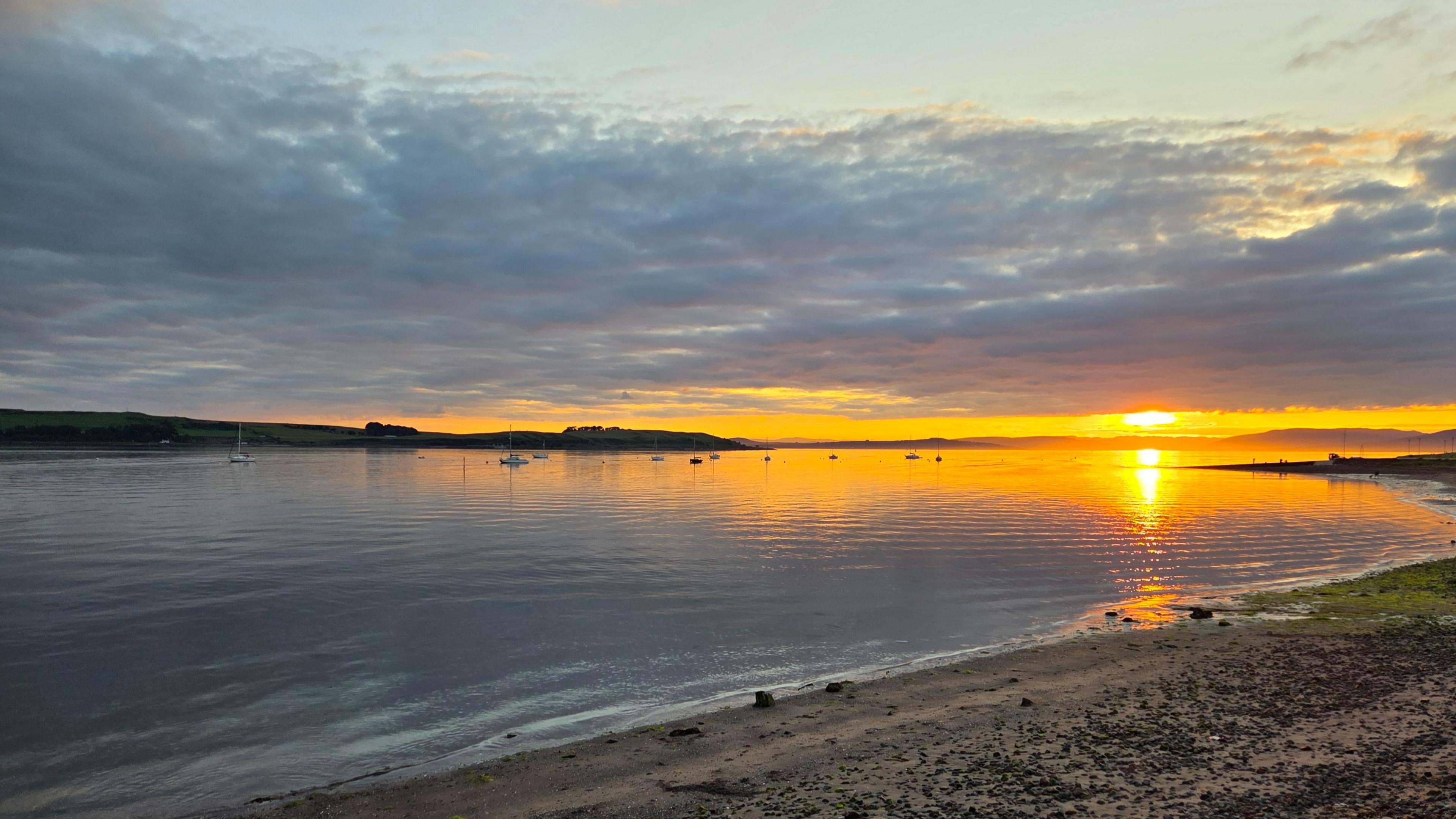 The sun sets over a beach and the sea in front of it.