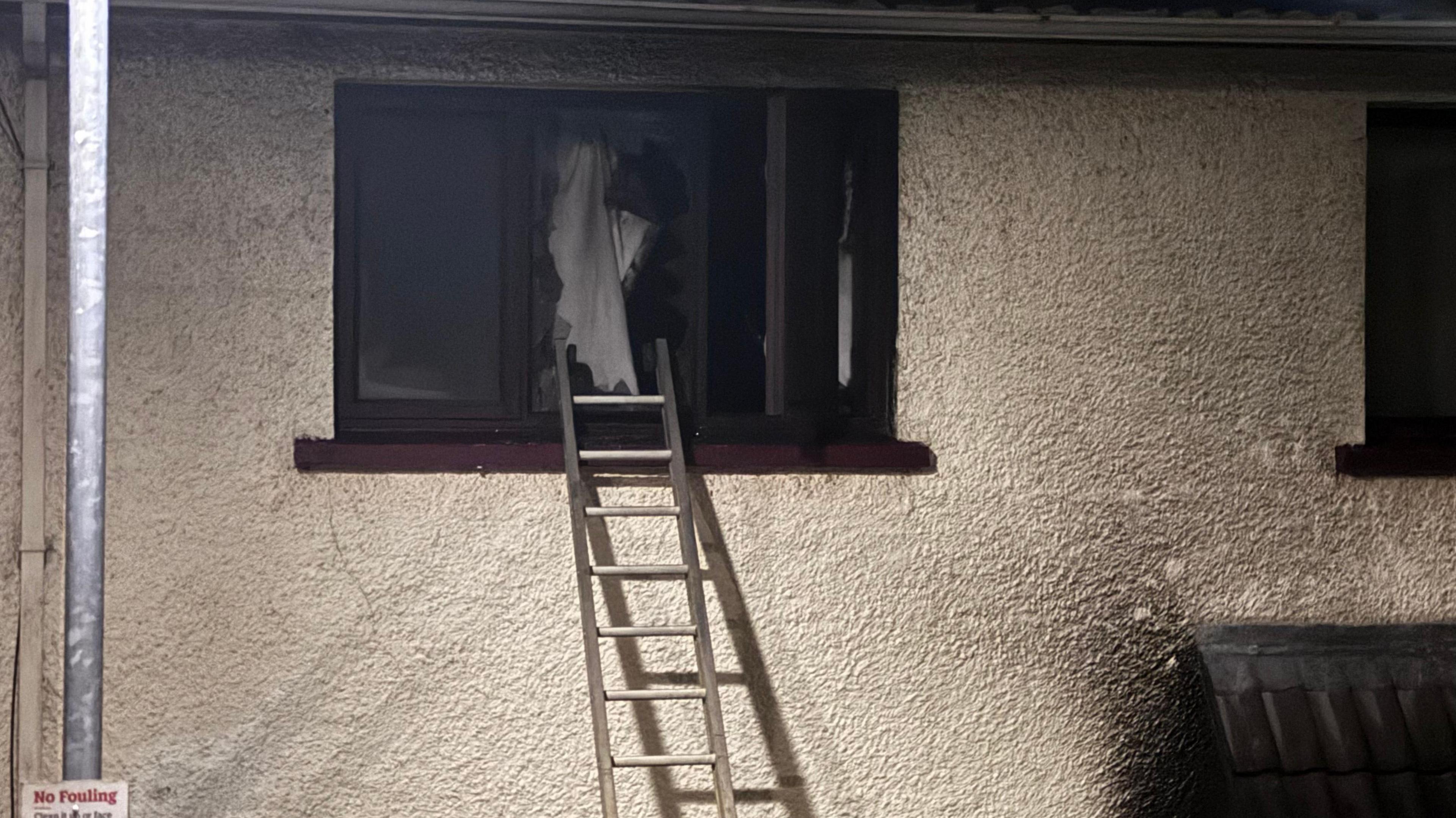 A burnt out upstairs window with  a ladder resting against it