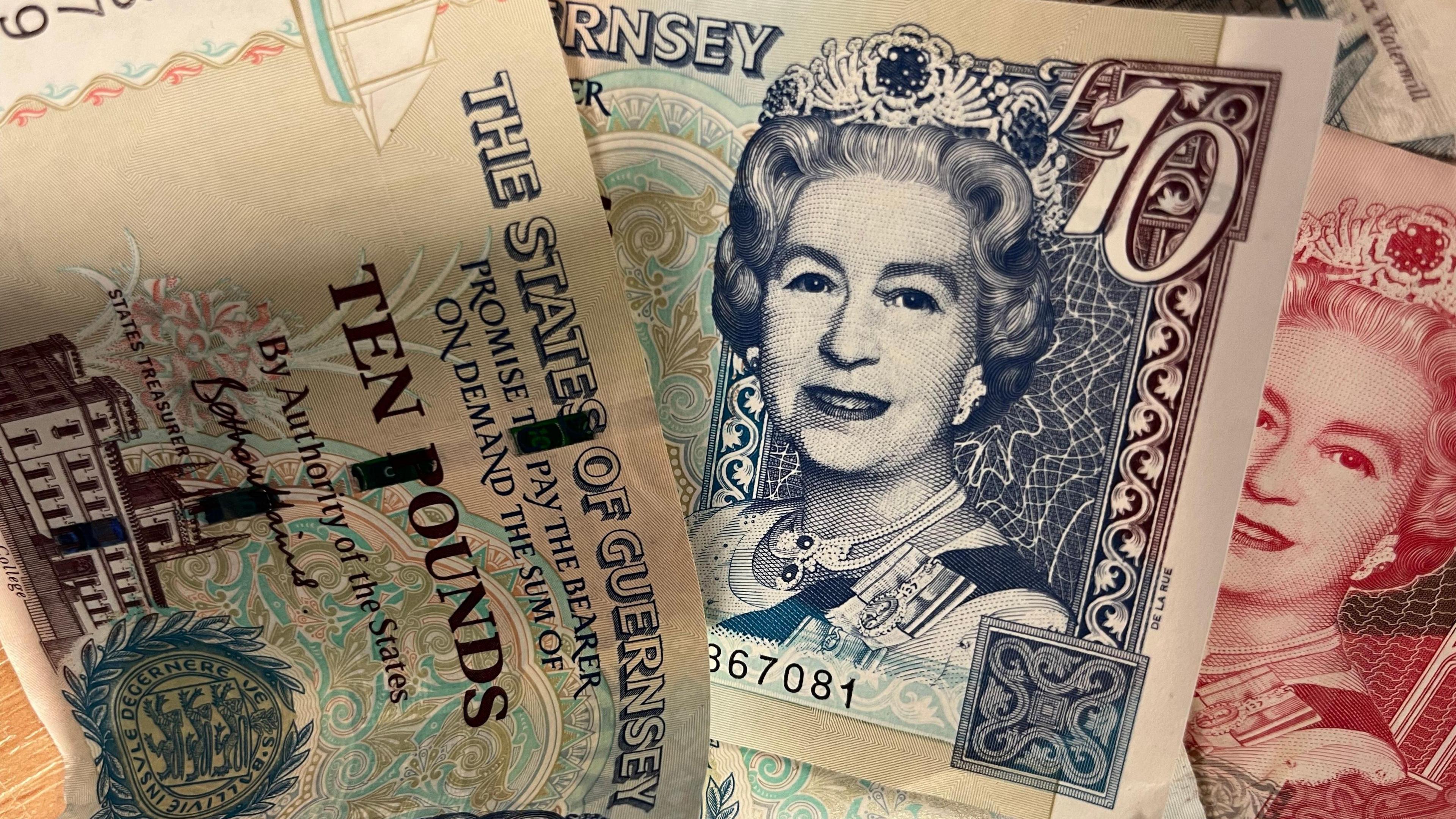 Three Guernsey ten pound notes lie flat on a table top.