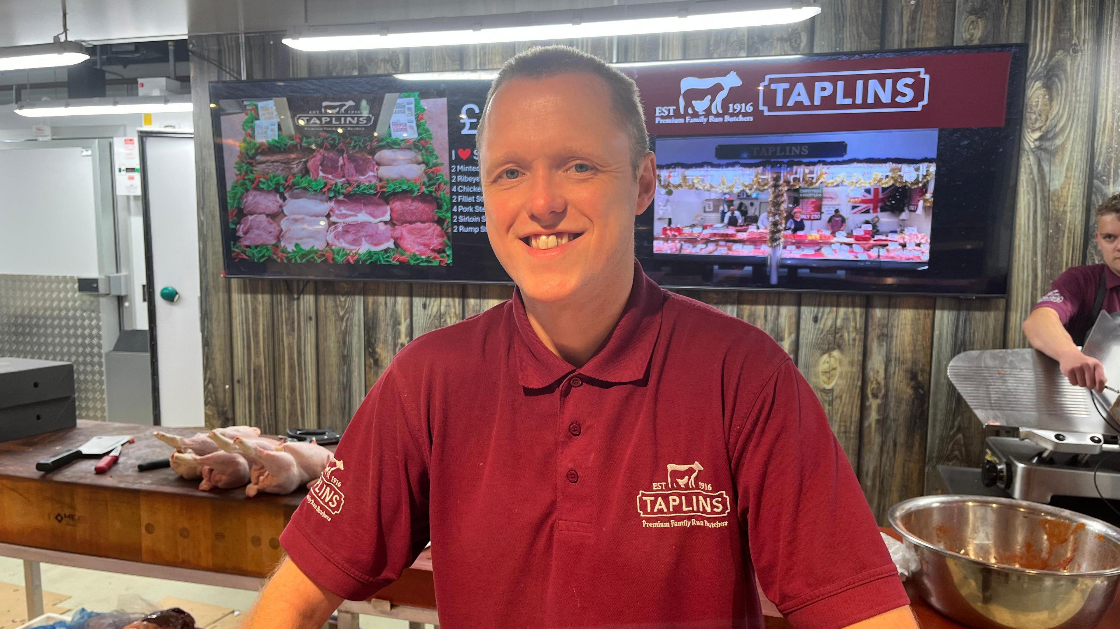 Man wearing Taplins shirt with butchers behind him.