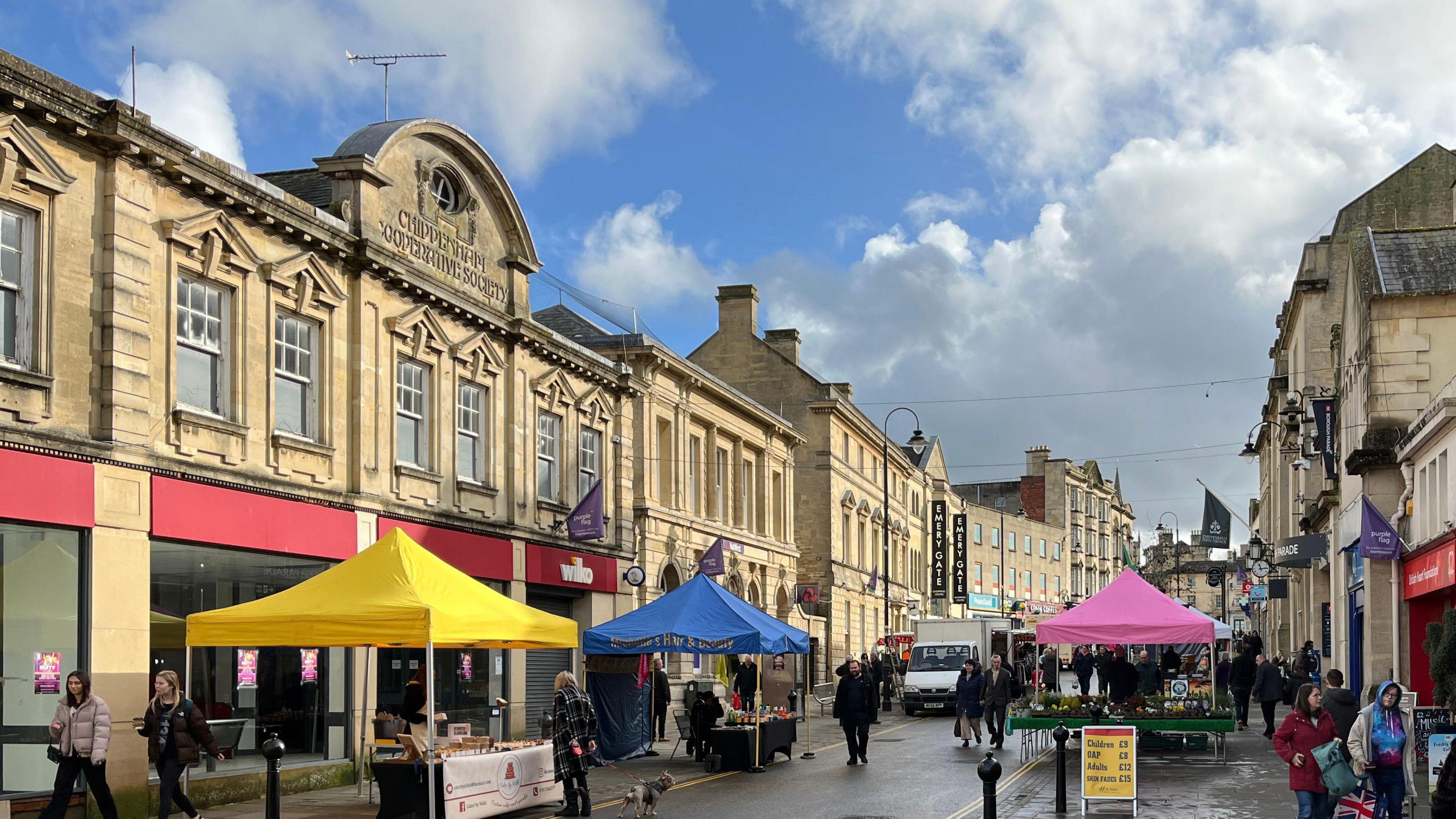 Chippenham High Street on a market day, lined with the light stone buildings with colourful gazebo tops down the middle