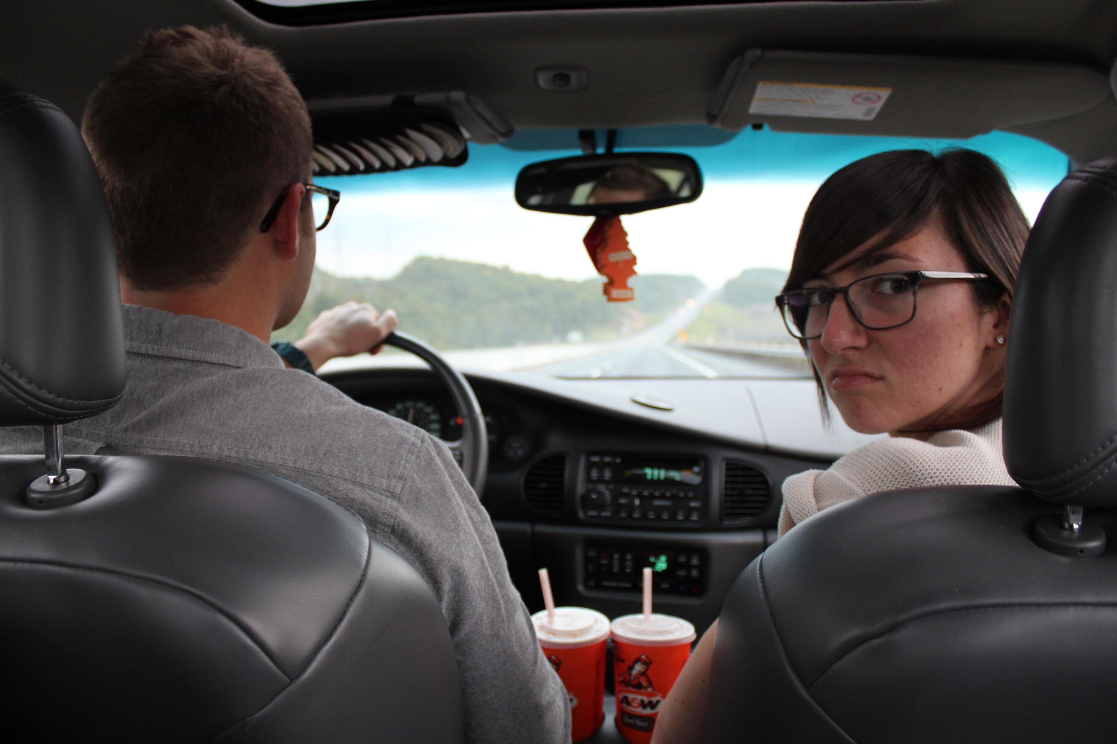 A woman in the passenger seat looks behind her while a man drives the car