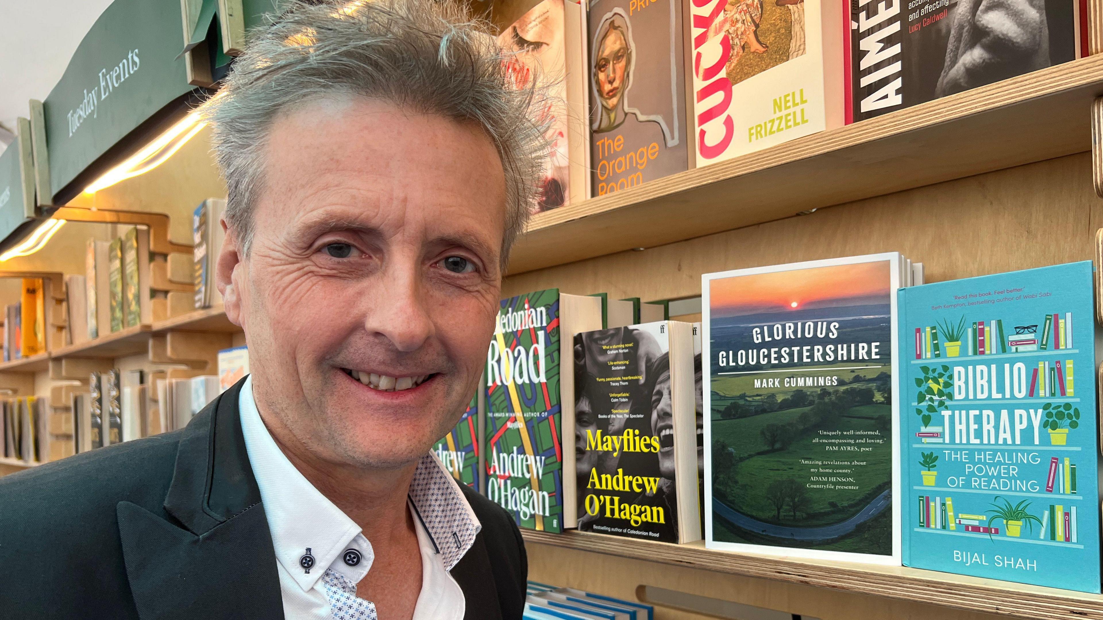 Mark Cummings smiles next to his book on a bookshelf