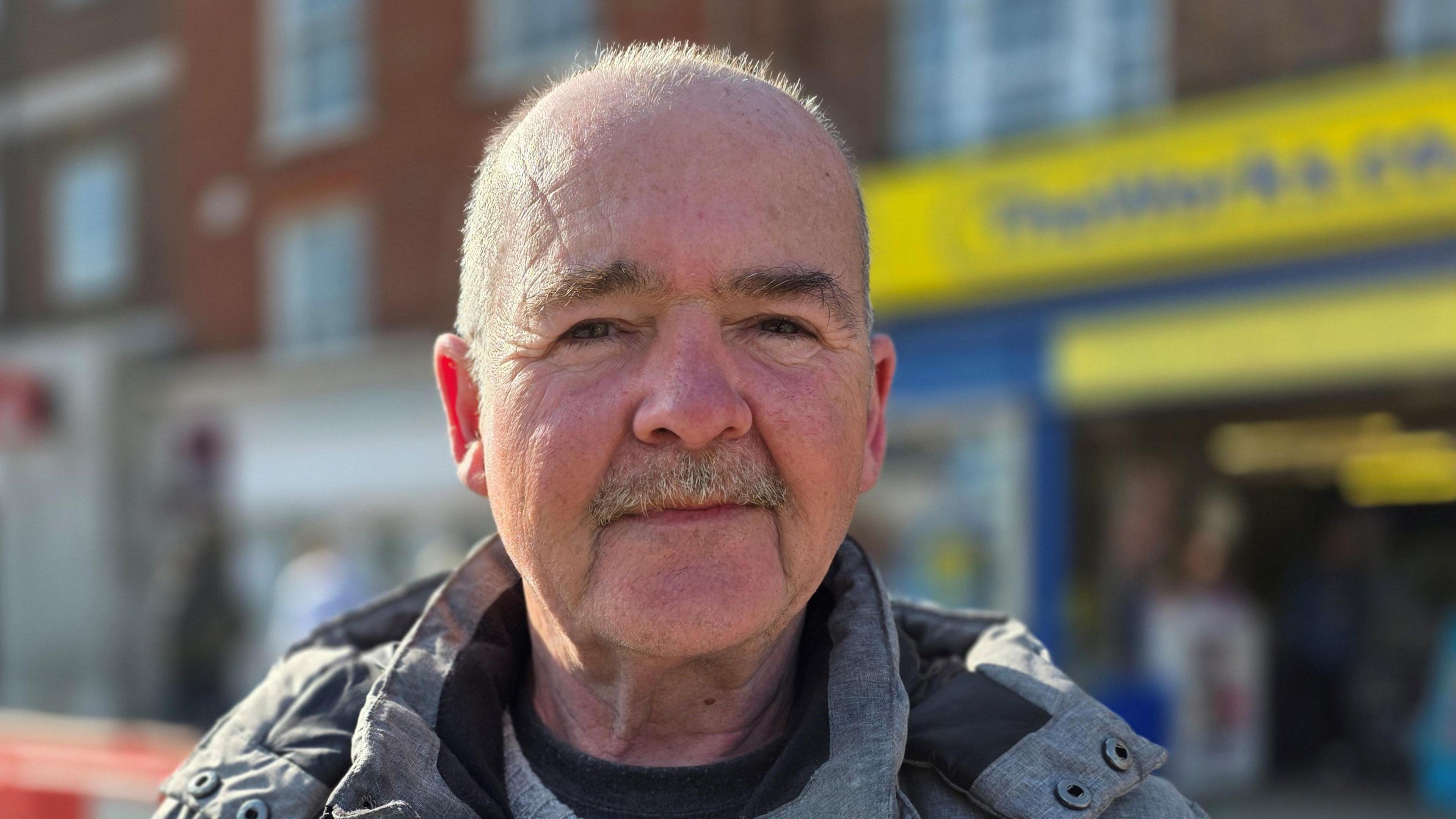 Gary Cooper is standing in front of a shop in Great Yarmouth. He's wearing a grey and black coat.