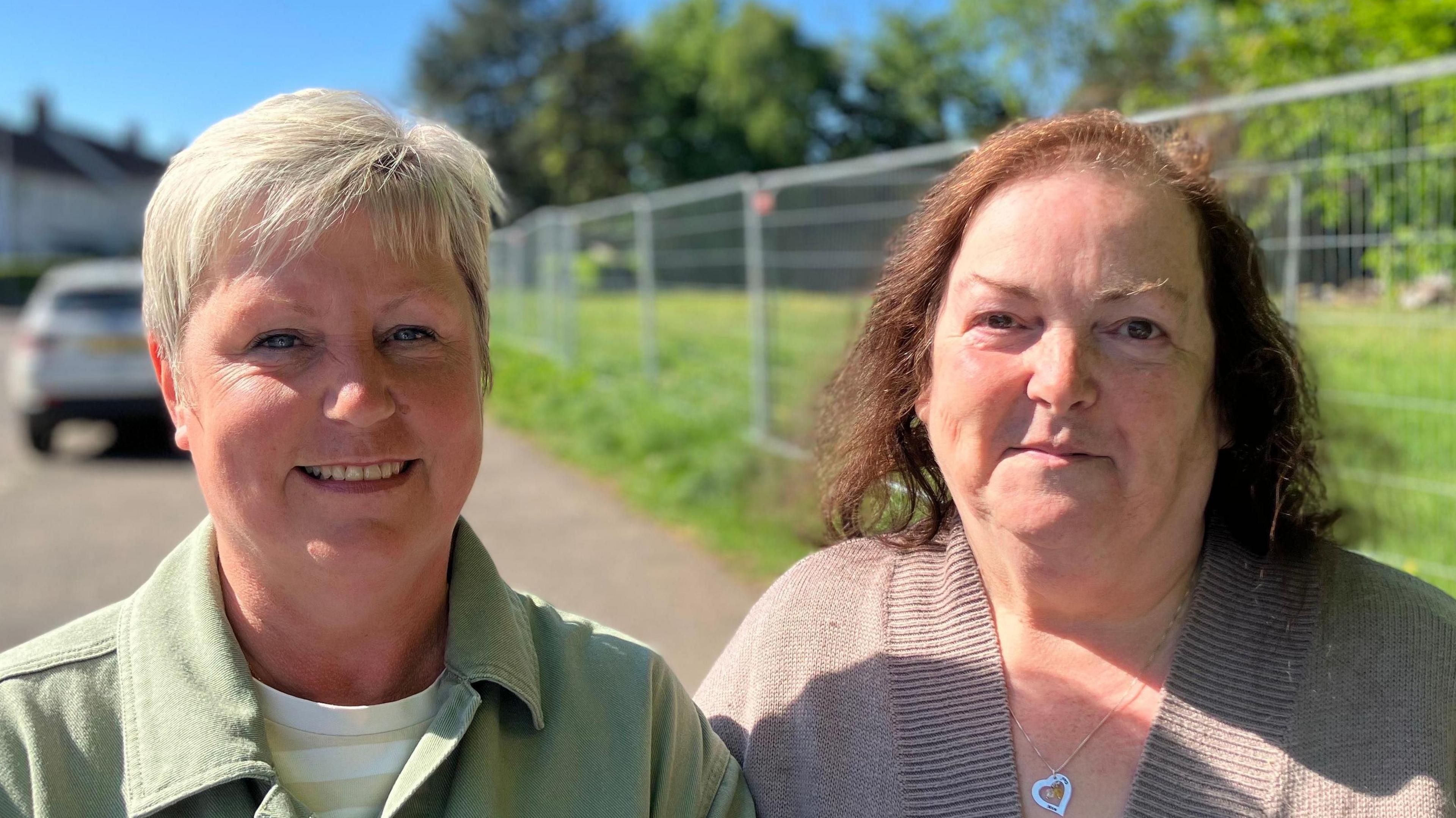 Alana Anderson has short blonde hair and has makeup on. She is wearing a green shirt jacket and a white t-shirt. Dorothy Anderson has long brown hair and is wearing a brown cardigan with a silver necklace. Behind them is a metal railing.