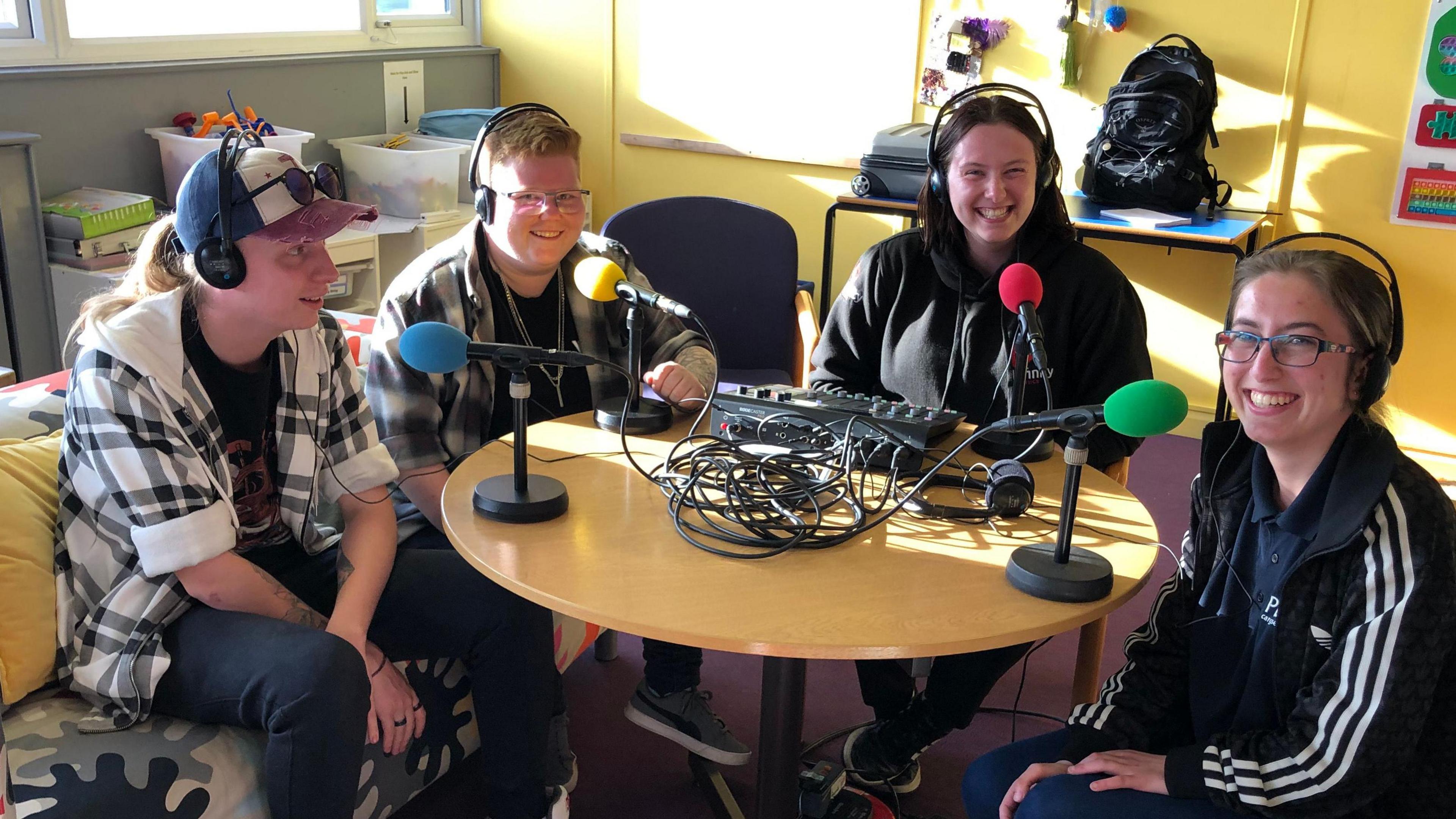 Four young people sit around a table with microphones