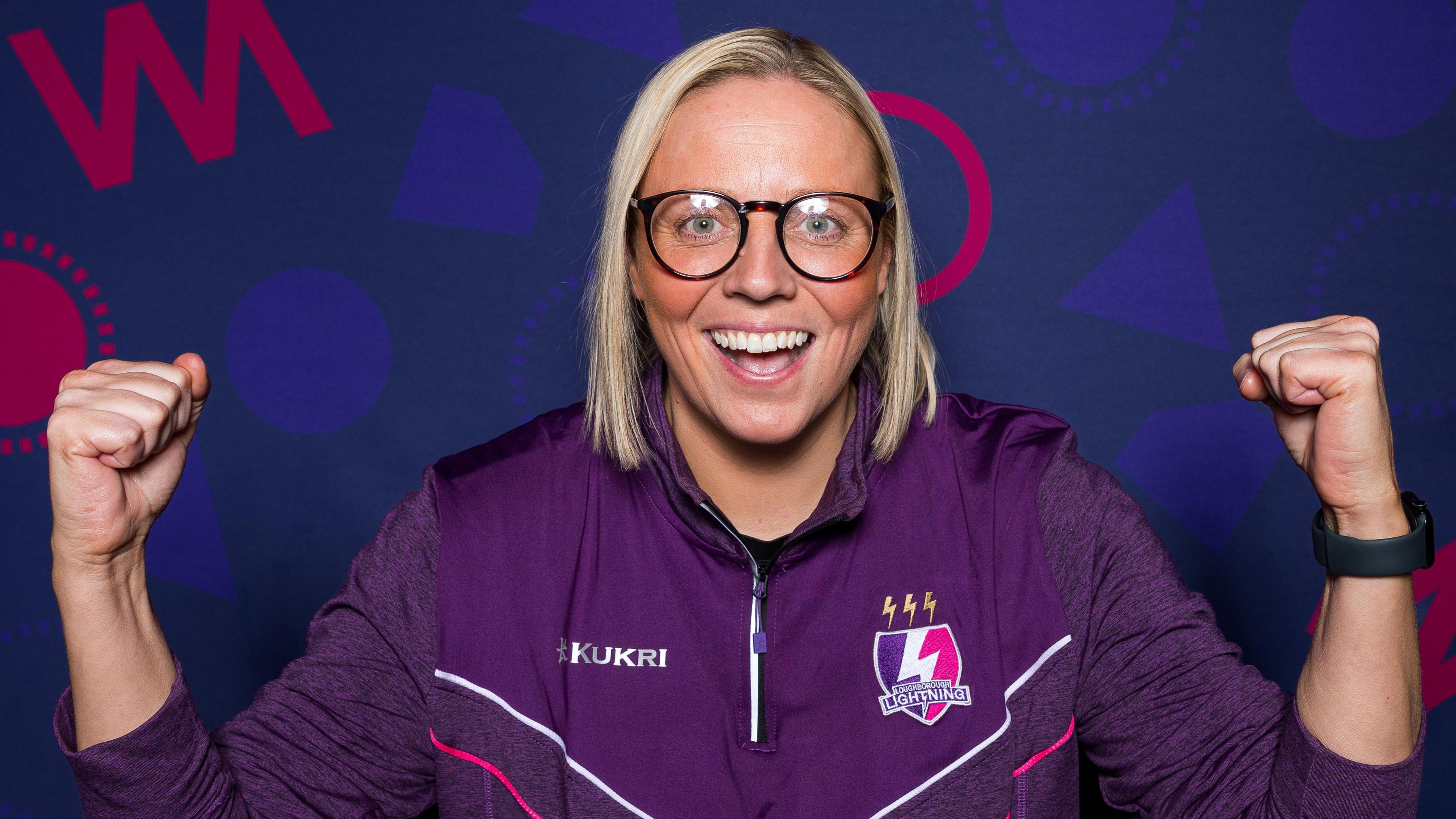 Blond-haired Vic Burgess smiling and cheering wearing glasses and her purple Loughborough Lightning training top.