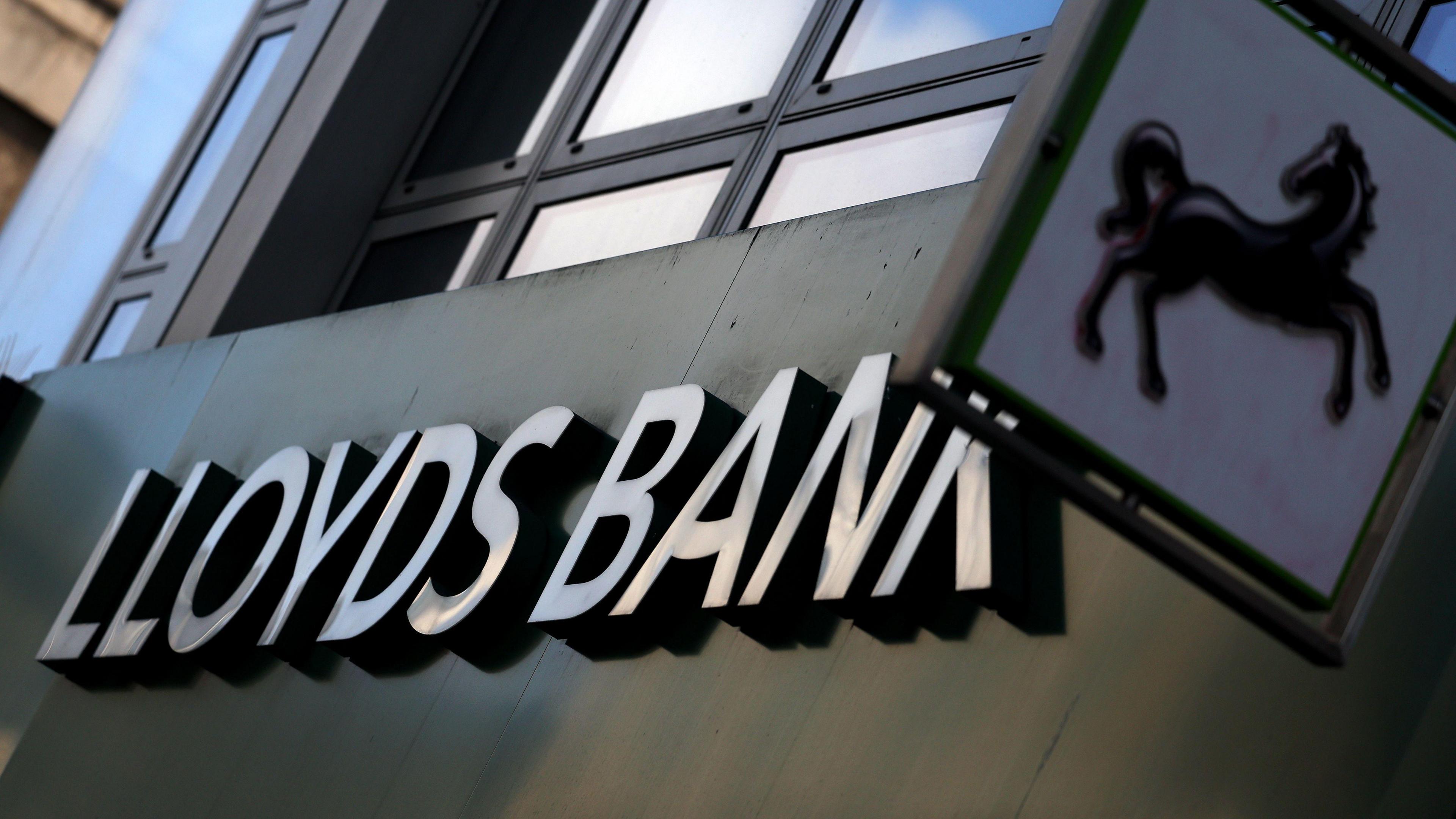 An exterior shot of a branch of Lloyds bank showing a sign with the bank's name and another smaller sign with it's logo of a black horse.