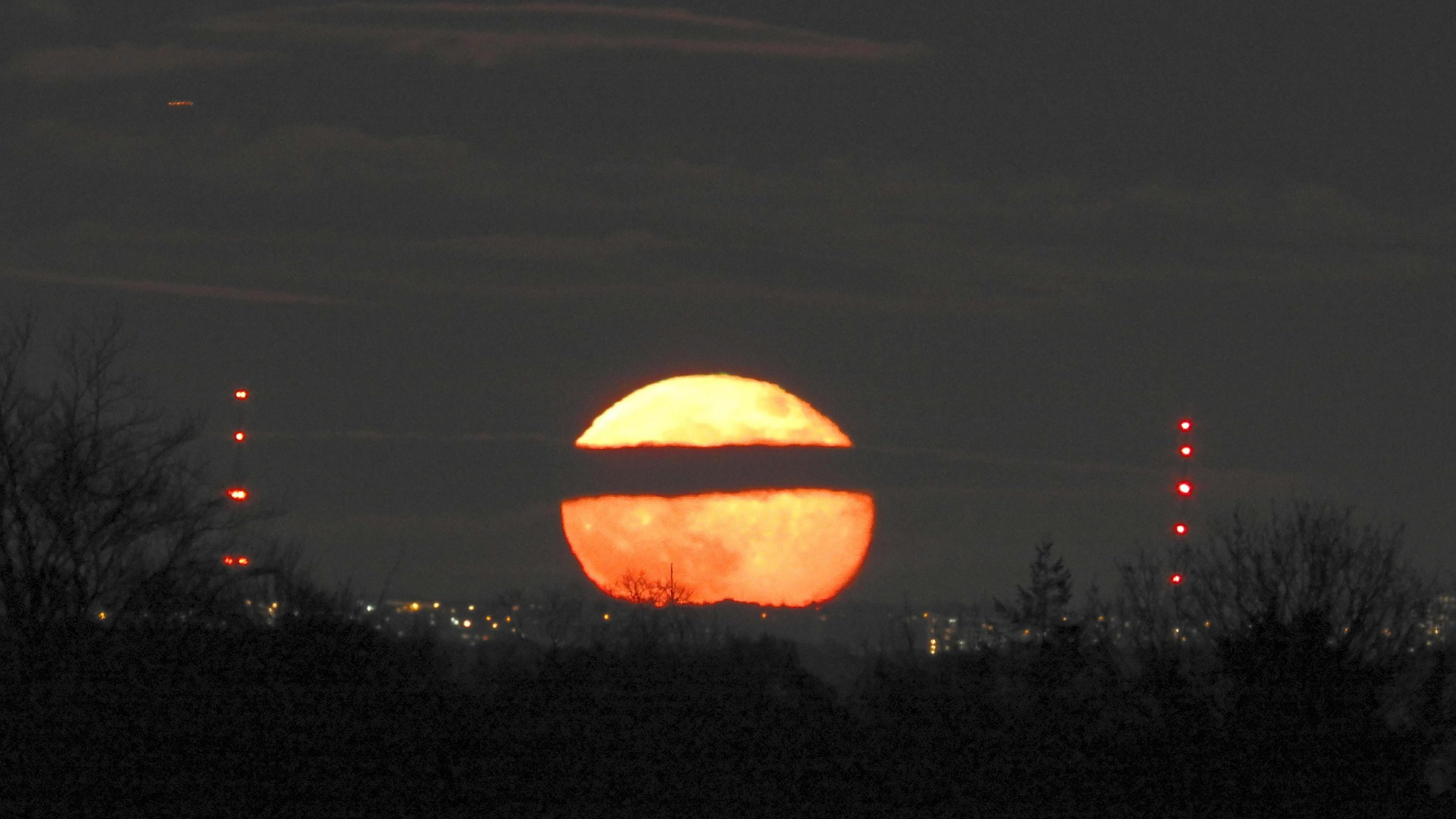 Orange Moon rising with a streak of cloud in front making it appear broken in two