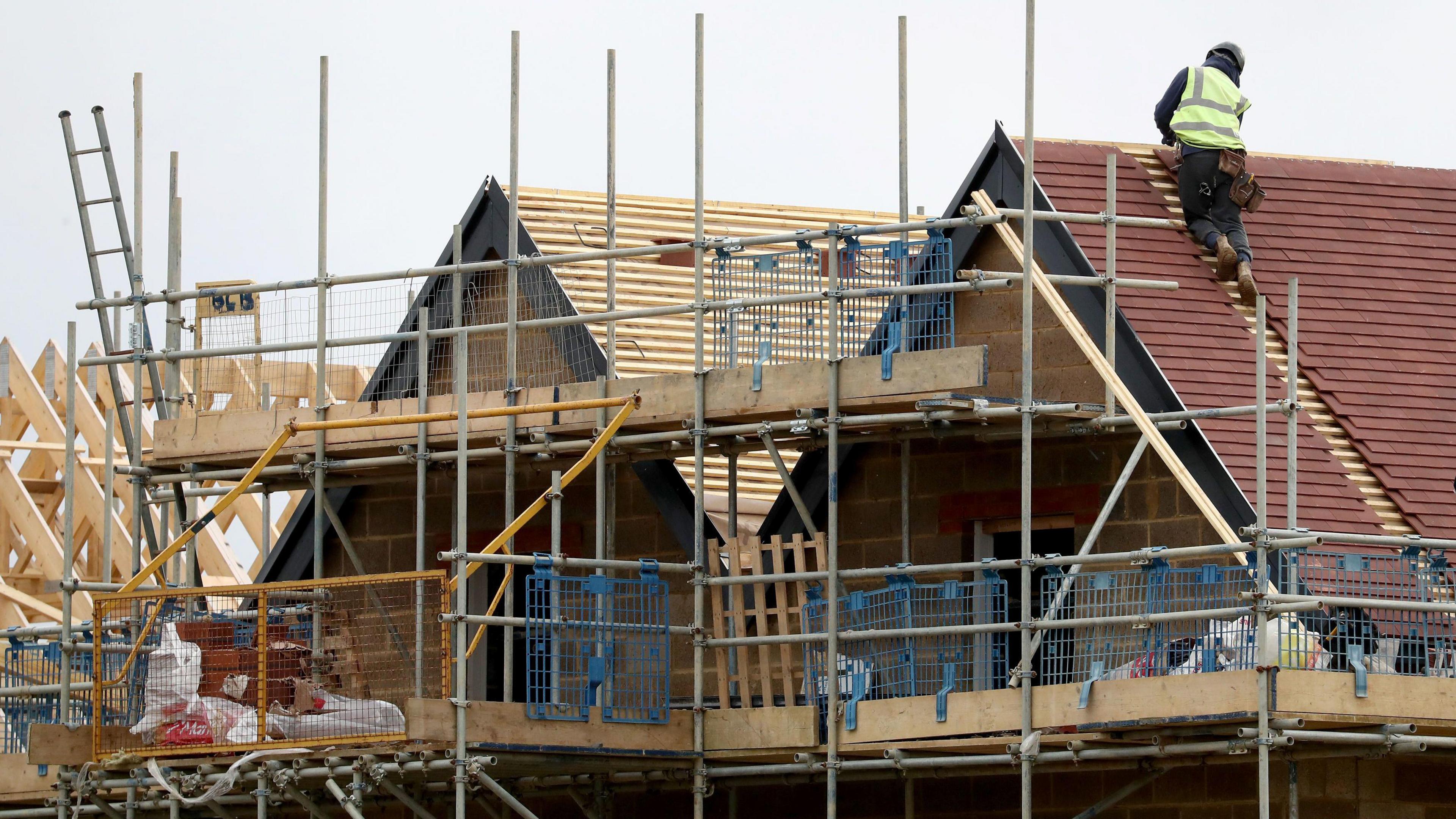 Builder wearing a high-vis jacket and a hard hat working on a roof of a house under construction