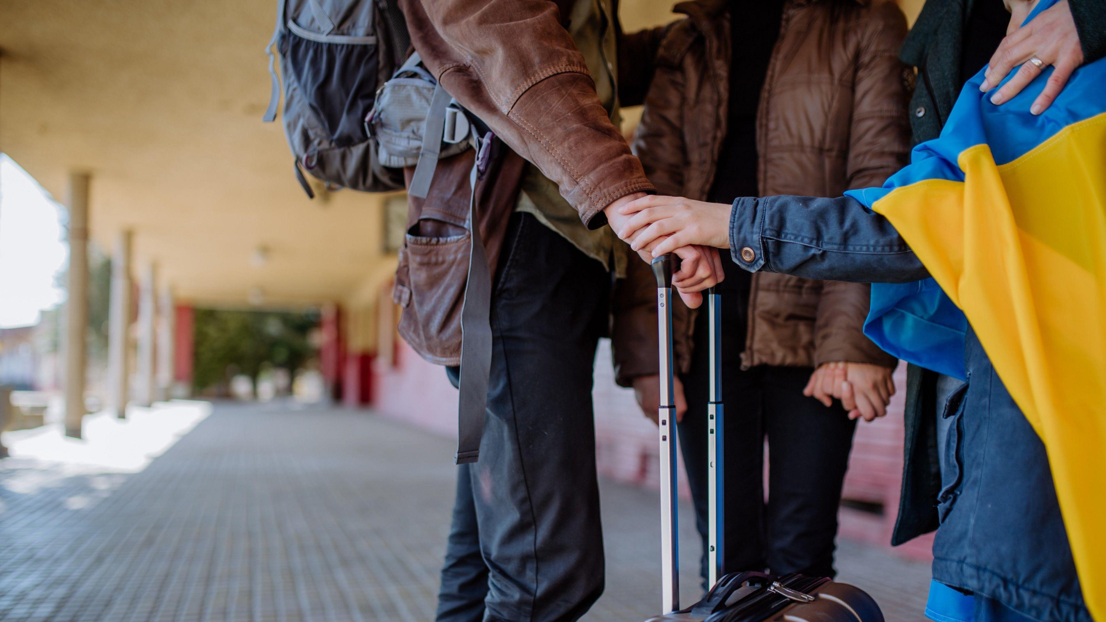 Low section of Ukrainian refugee family in station waiting to leave Ukraine due to the Russian invasion of Ukraine. They stand around a suitcase with its handle pulled up.  