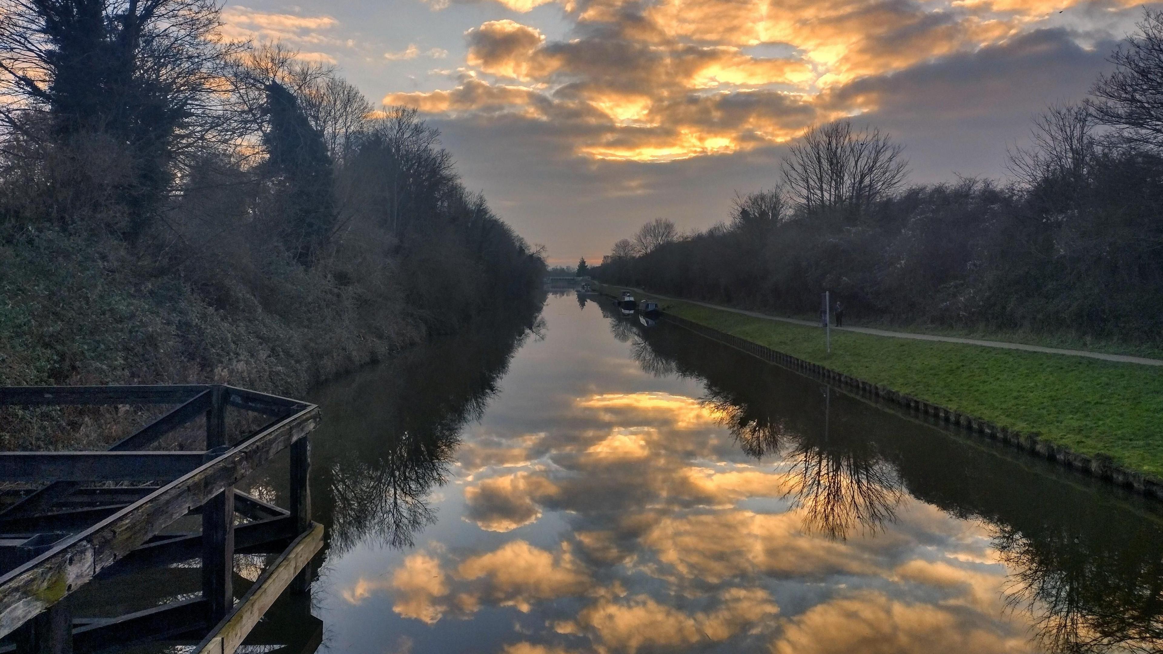 A group of clouds reflecting in the river at Quedgeley. The water is calm and along both sides there is grass and trees