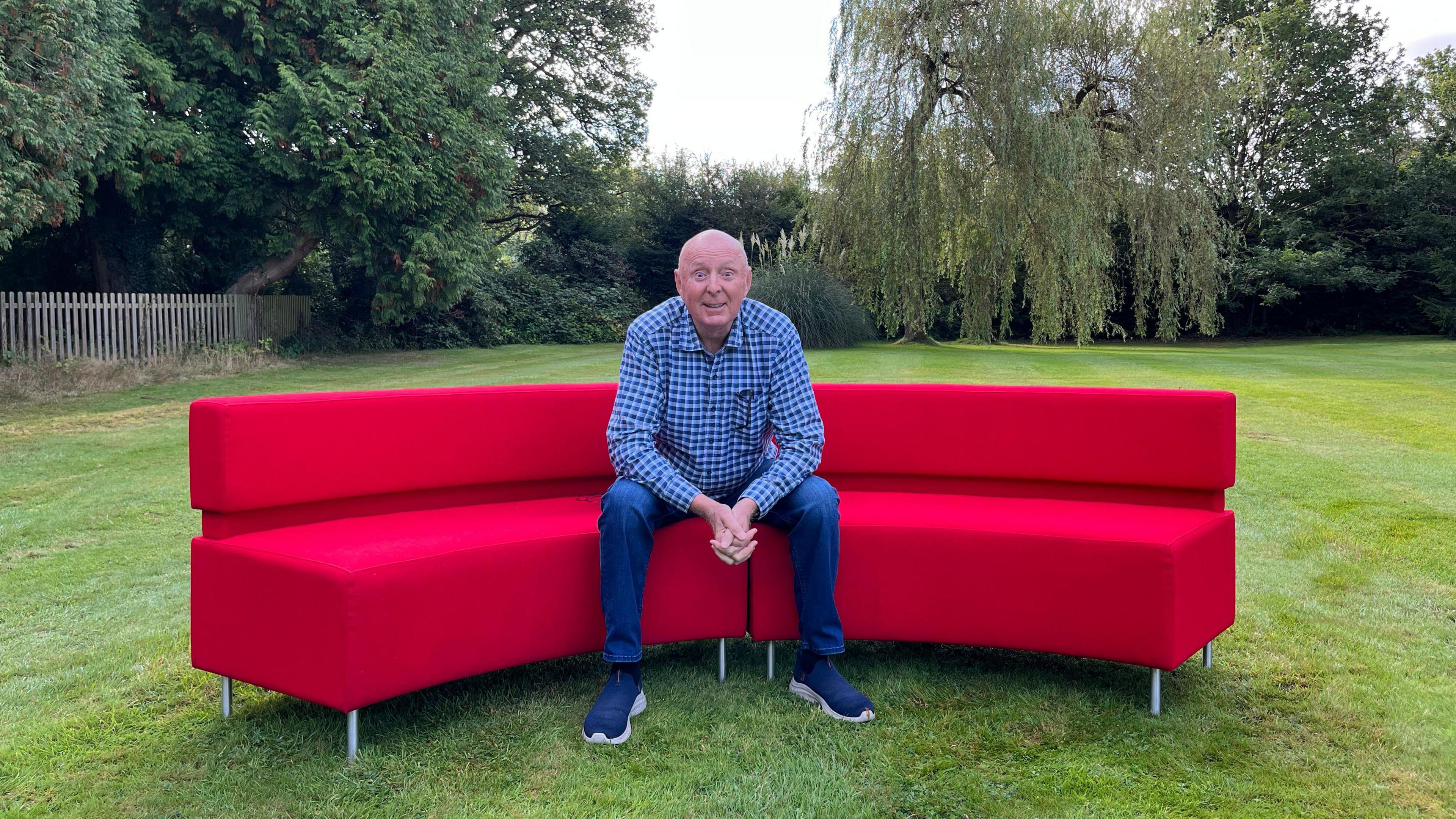 The comedian Jasper Carrott sitting on the red sofa in his garden in Warwickshire