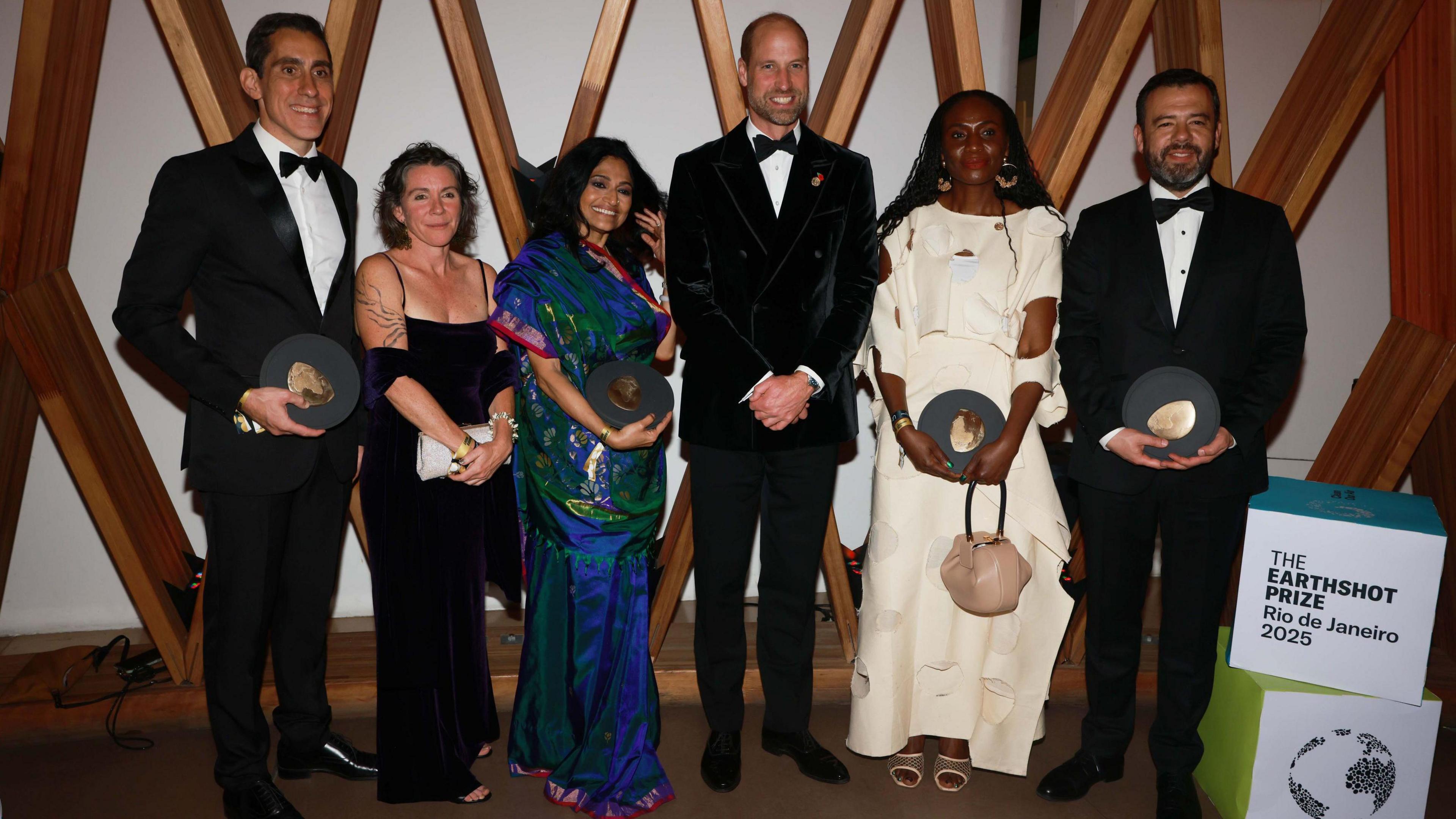 Winners of the Earthshot Prize stand with Prince William holding their awards and smiling at the camera