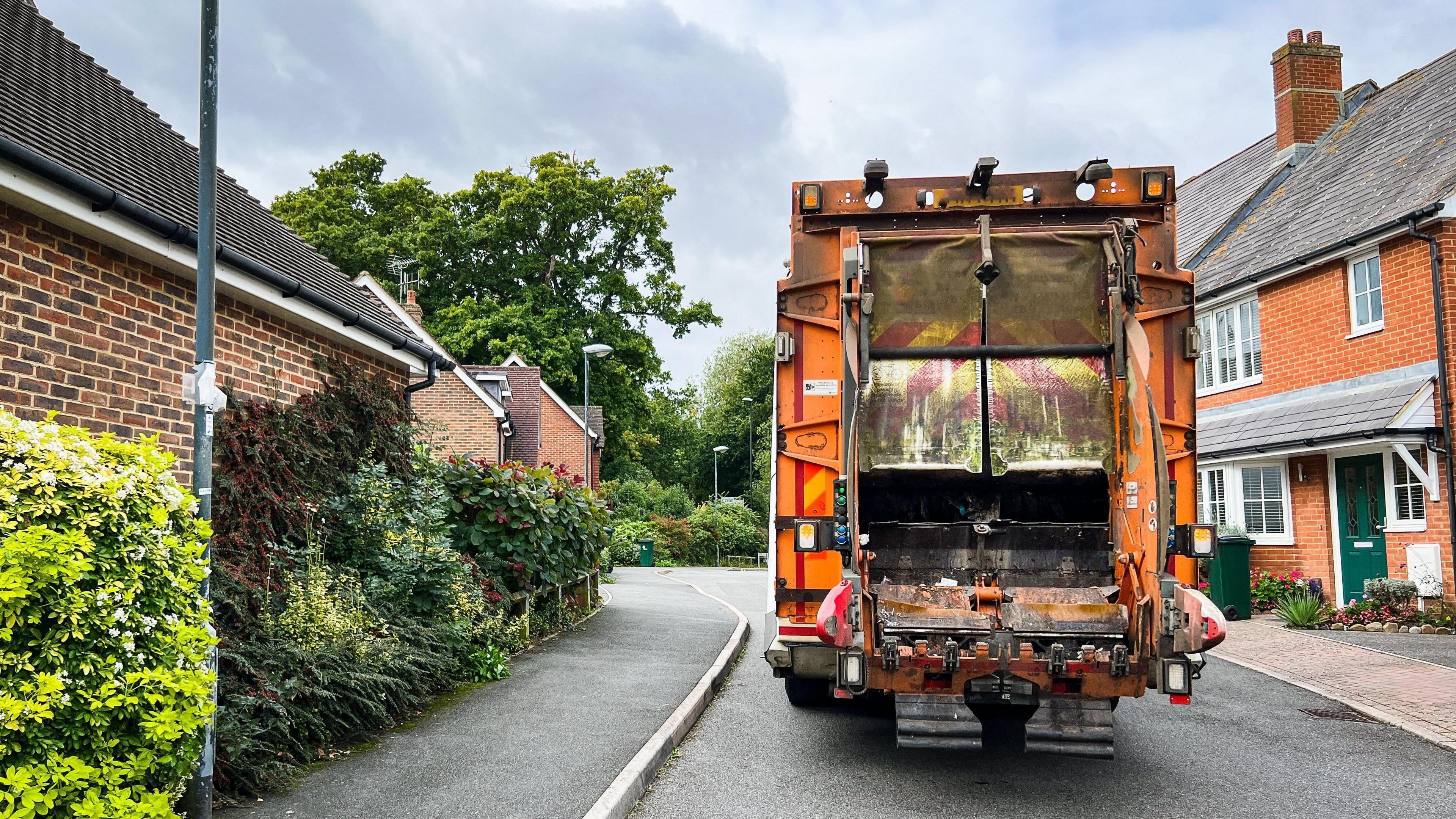 A generic image a orange waste lorry on a residential street.