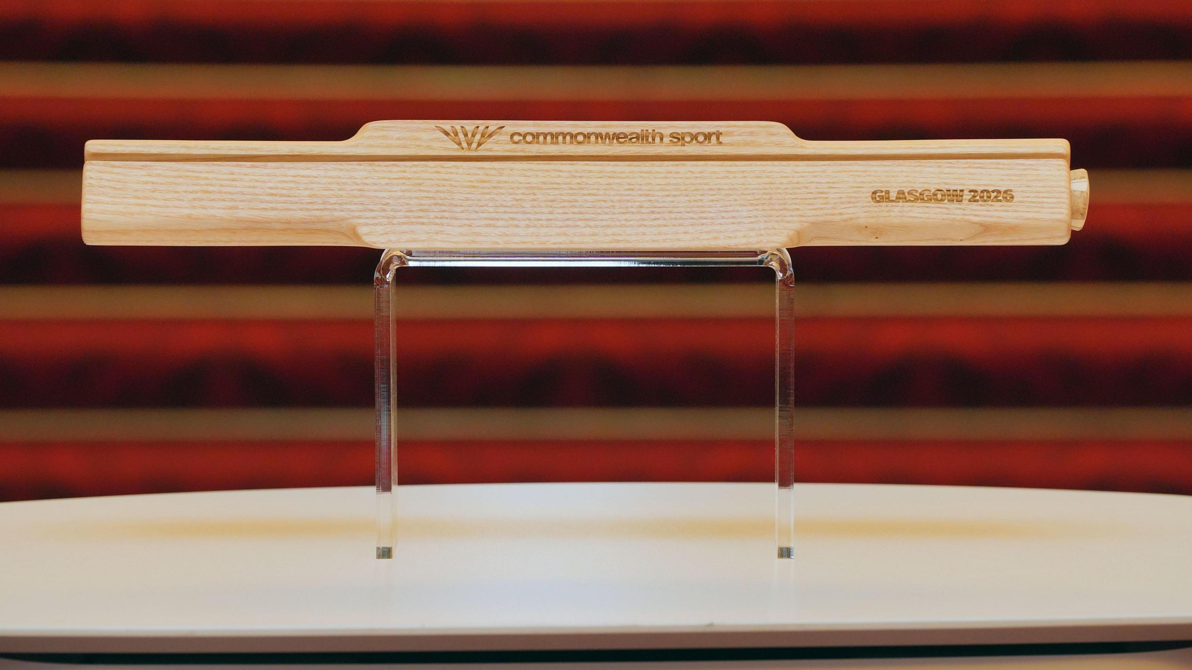 The wooden baton sitting on a plinth. It has the words Commonwealth Sport and Glasgow 2026 carved into it