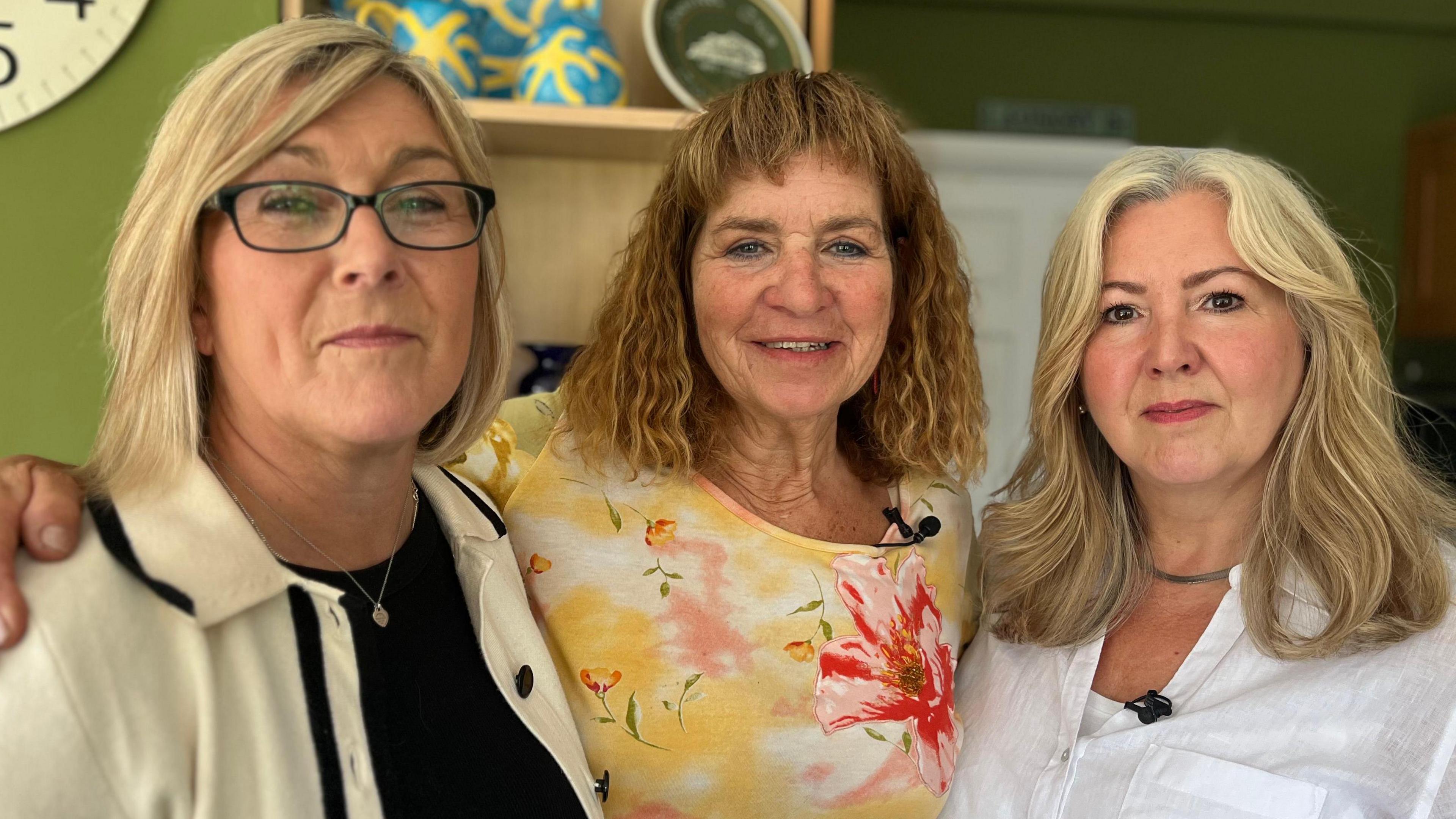  Helen, Amanda and Joanne. Helen has blonde bobbed hair and is wearing glasses, a cream and white jacket and a silver pendant around her neck. Amanda has curly brown shoulder-length hair with a  fringe and is wearing a yellow and pink floral top. Joanne has shoulder length blonde hair and is wearing a white shirt.
