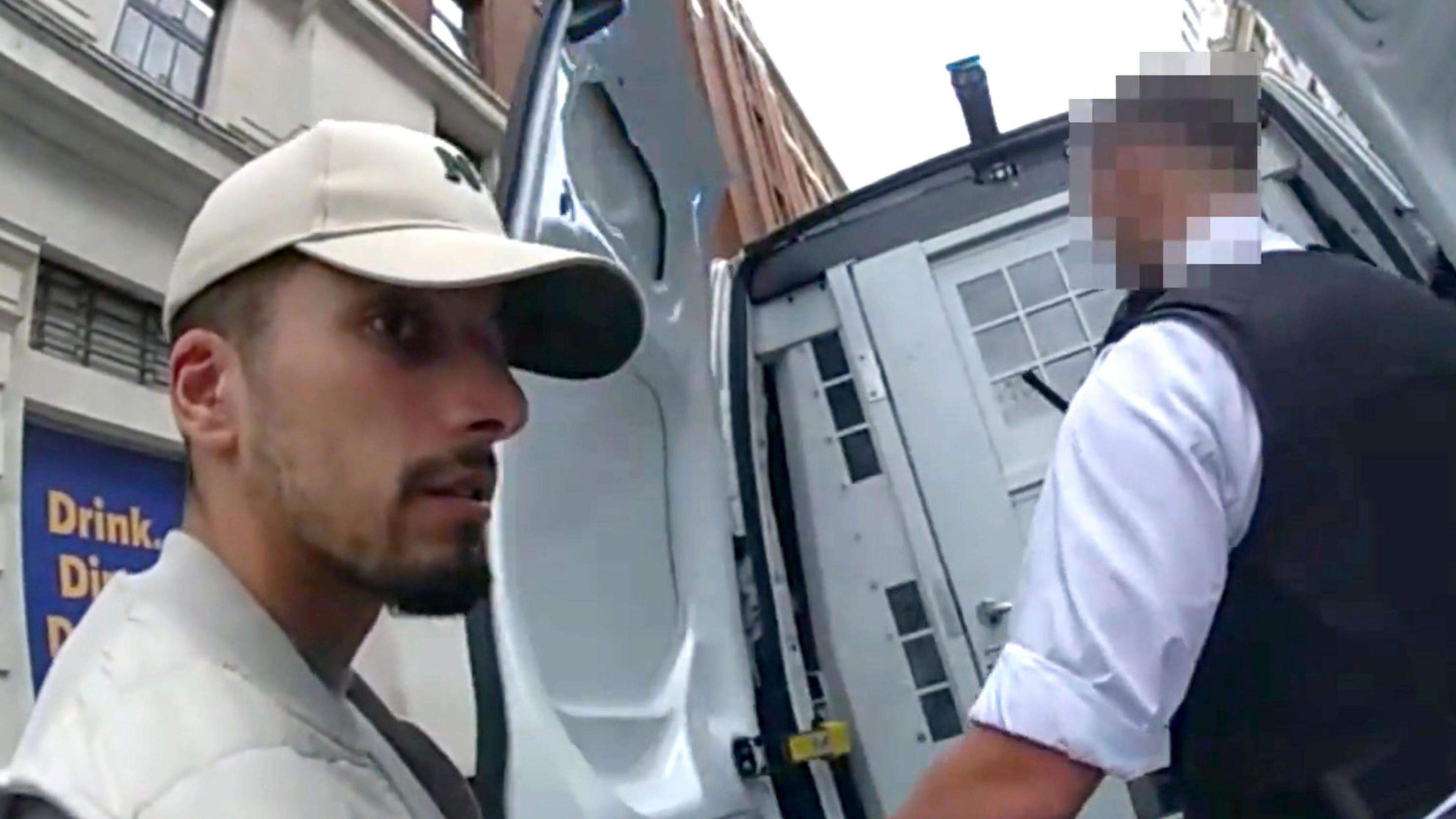Handout body worn camera video grab issued by the Metropolitan Police dated 09/09/25 of the arrest of 24-year-old Algerian national Brahim Kaddour Cherif - he has a goatee and is wearing a baseball cap, being led into the back of a police van