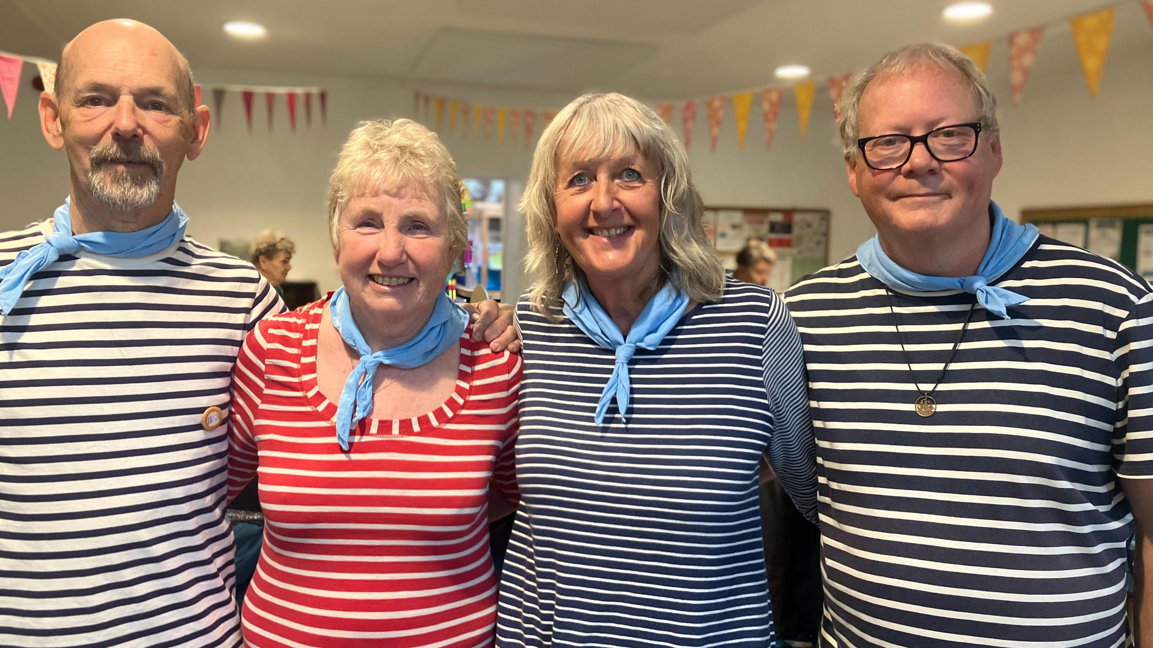 Four people stand in stripes sailor tops with blue neckerchiefs wrapped around their necks.
